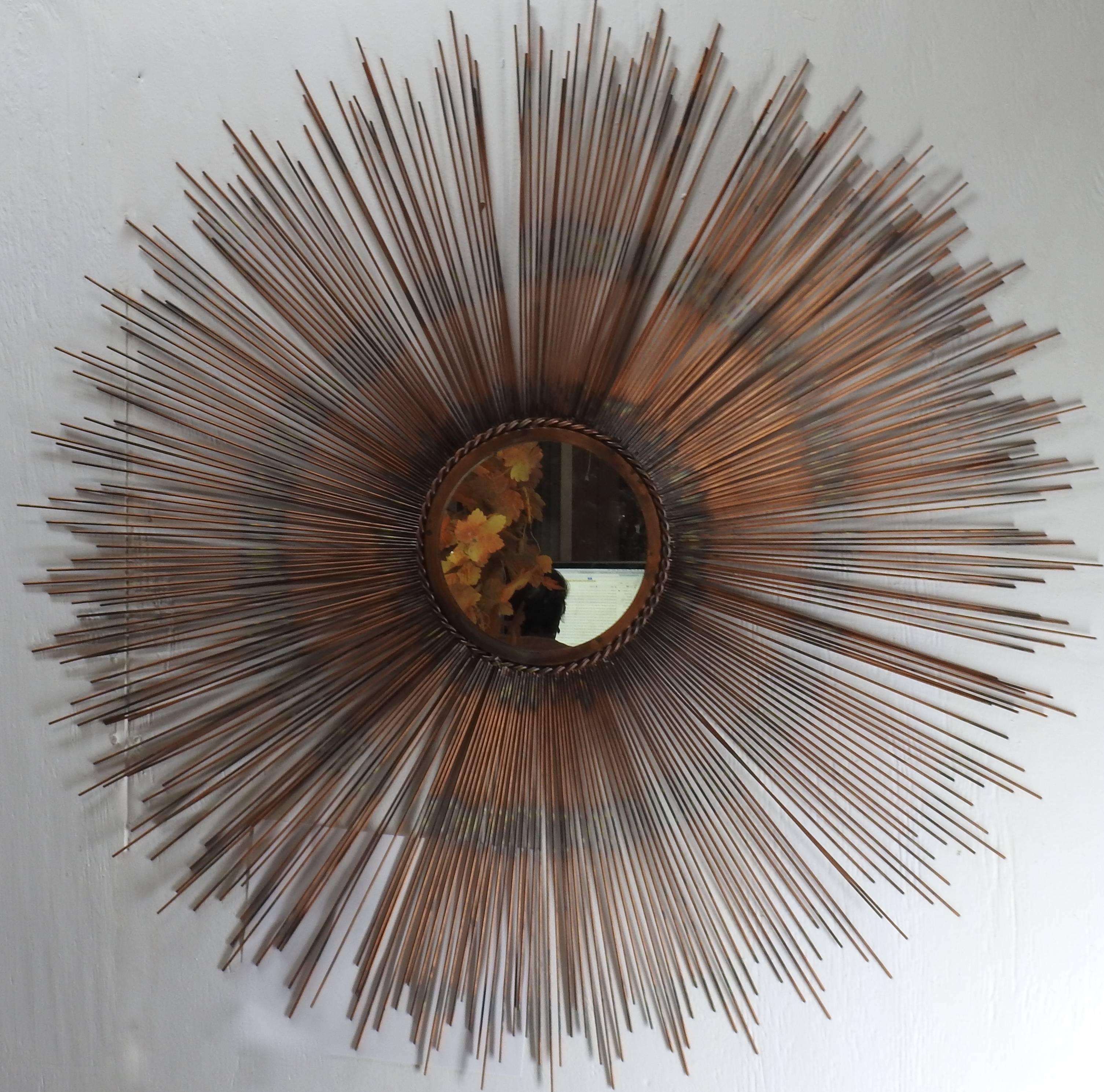 The sunburst on this stunning mirror showcases shades of copper on the metal. The mirror is framed with a twisted metal border. The centre mirror has a hanger mounted to the back which is finished with black felt.