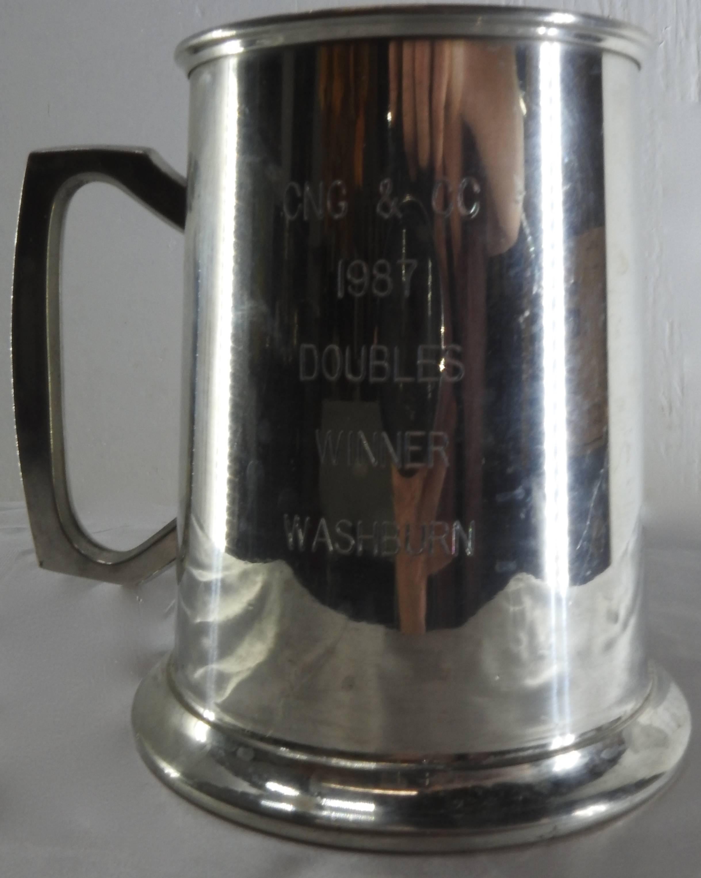 Featured is an engraved pewter tankard which was made in Bolivia. It has Classic lines formed in the pewter and the bottom is enclosed in glass. The engraving states CNG & Co., 1987, Doubles Winner, Washburn. The bottom is stamped genuine Pewter