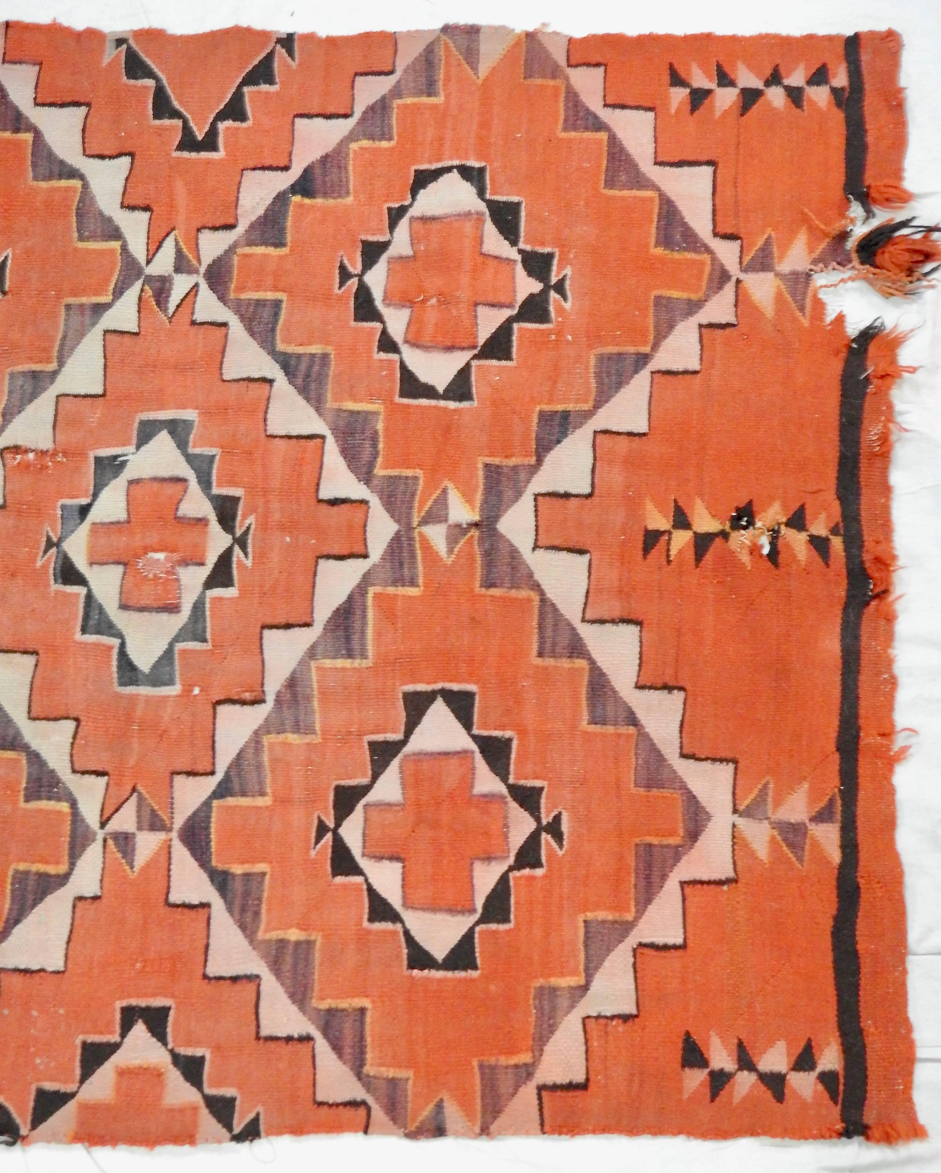 This is an antique handwoven Navajo transitional textile, circa 1900. This antique wool rug features a Native American design after a Ganado pattern of stepped diamonds, cross-shapes, and hooks over a red ground. Rendered in a palette of red, mauve,