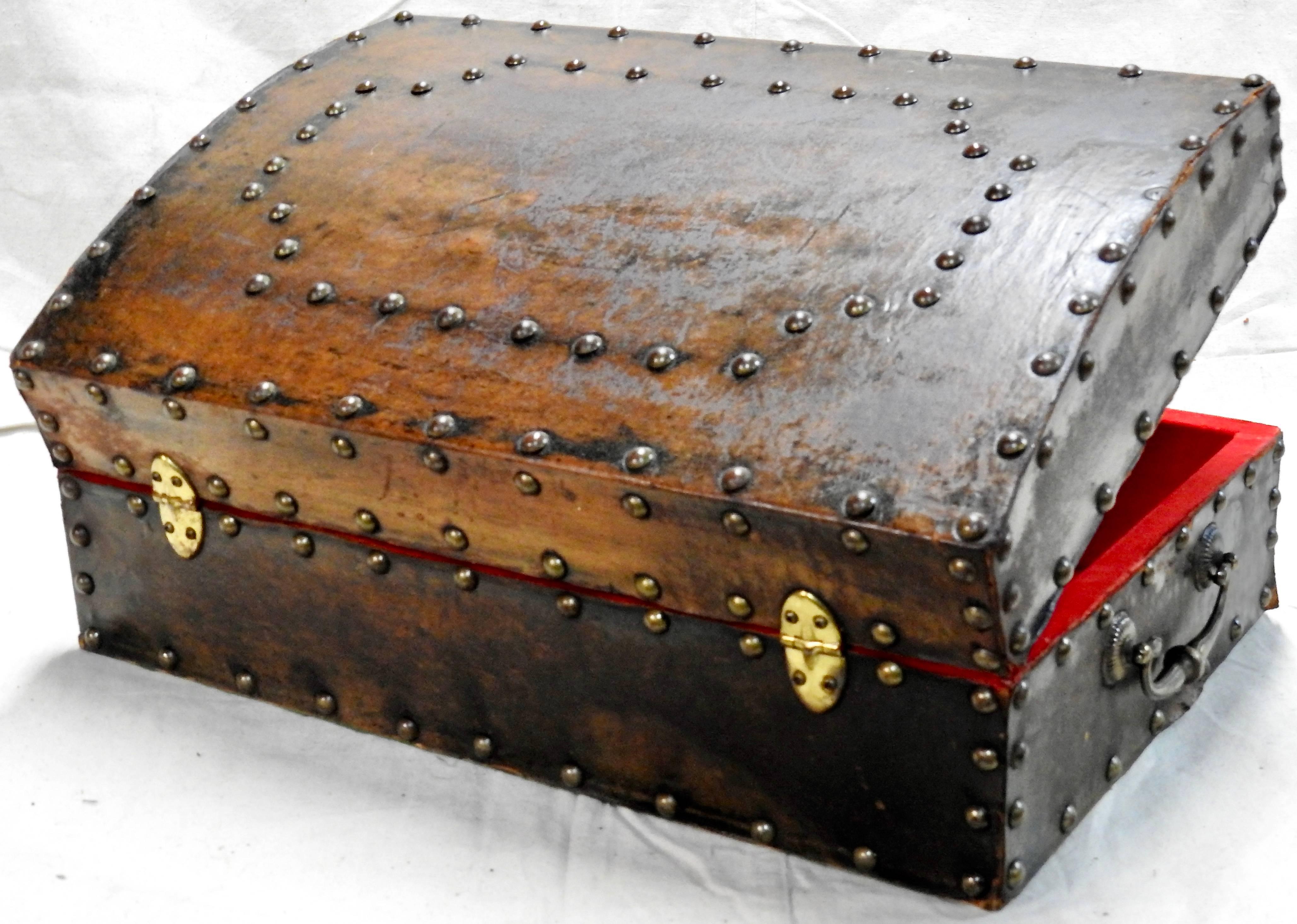 The hammered bronze tacks make a statement on this Classic leather on wood box from the late 1800s. It has a pair of bronze handles for easy lifting. The curved top is enhanced with additional tacks. The red fabric lining the interior is velveteen