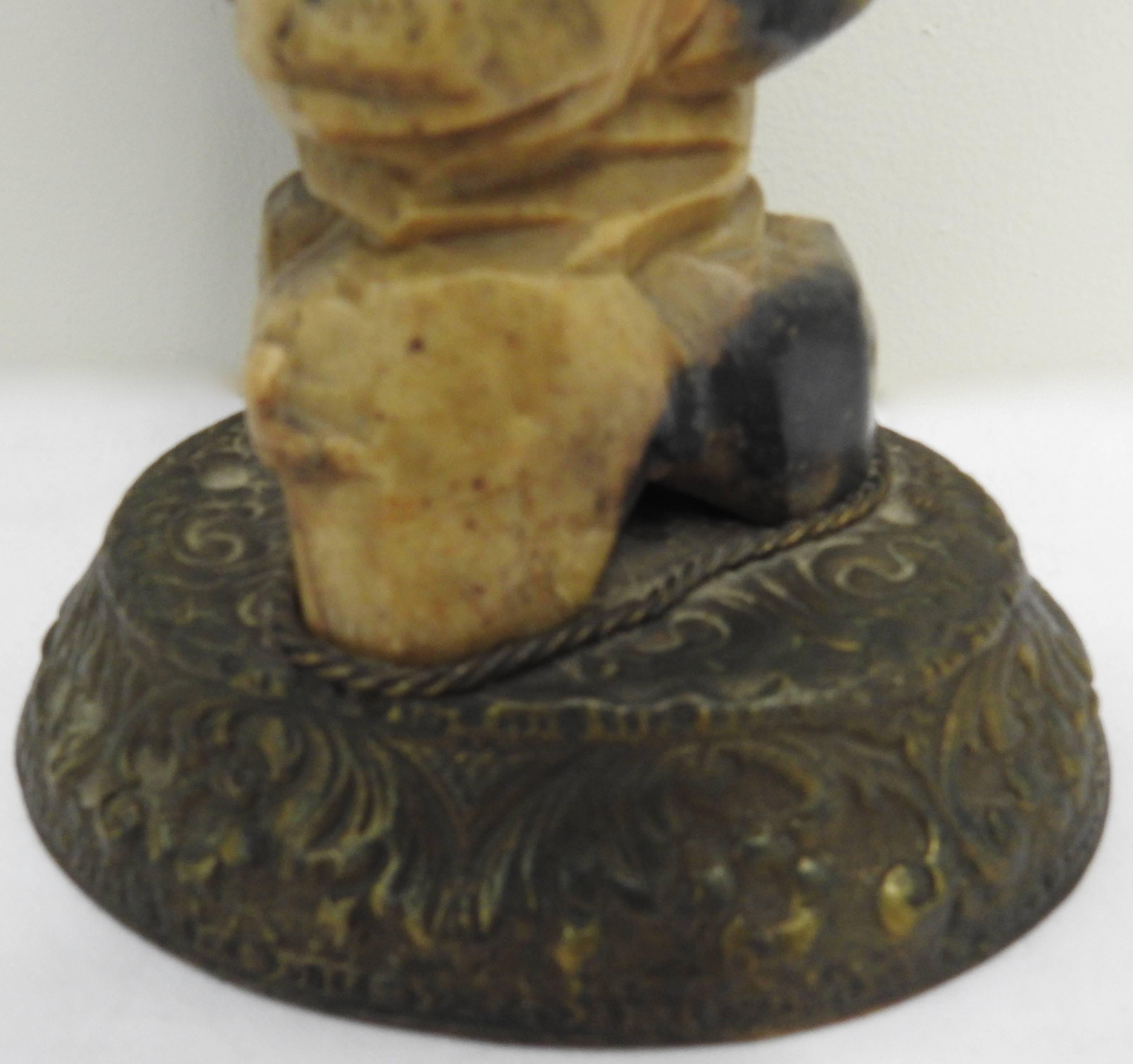 This hand carved soapstone figure of a bearded man holding a fish in one hand and a staff in the other will make you smile. He appears to be grinning at you! He is perched on two rocks which are mounted to an exquisitely bronze cast base. The base