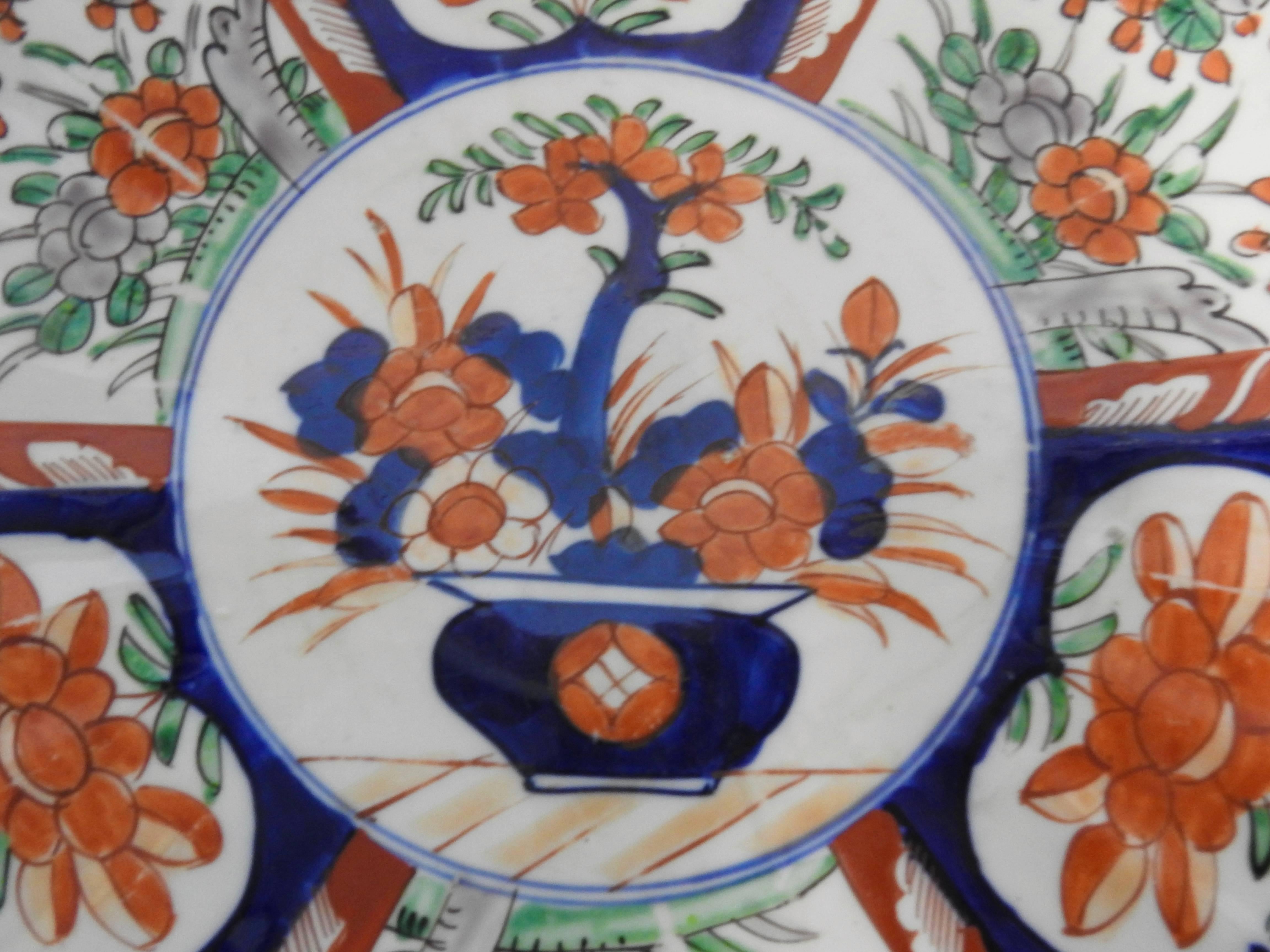 Smooth scalloped edges surround the beauty of this Japanese Imari plate from the early 20th century. Vibrant shades of red, blue and green have been expertly hand painted on the white porcelain. The back of the plate has blue artwork.