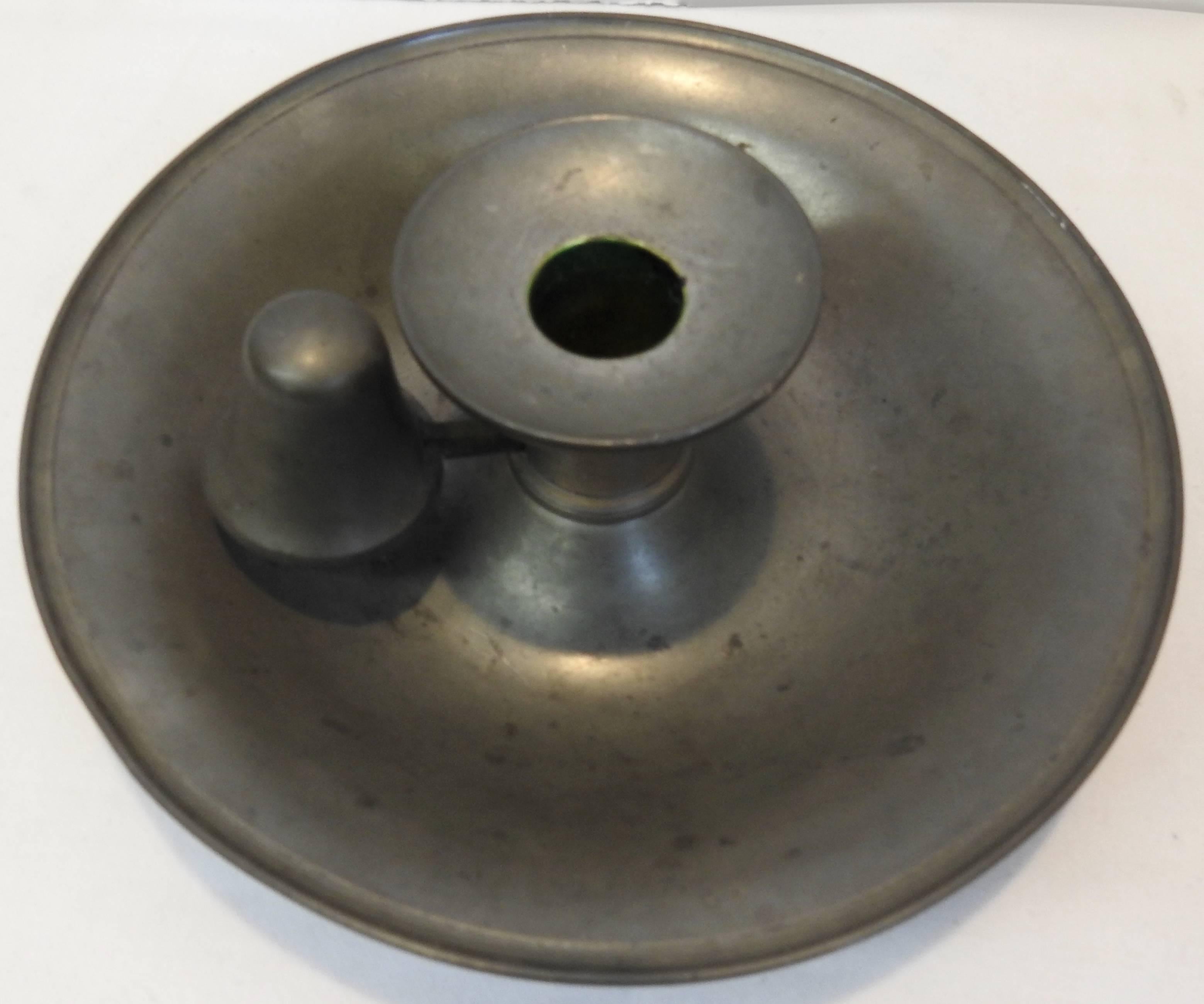 Featured is a unique candlestick saucer in the Colonial style. The part that holds the candle lifts up so you can easily carry the candle by the handle. Beautiful patina on the pewter.