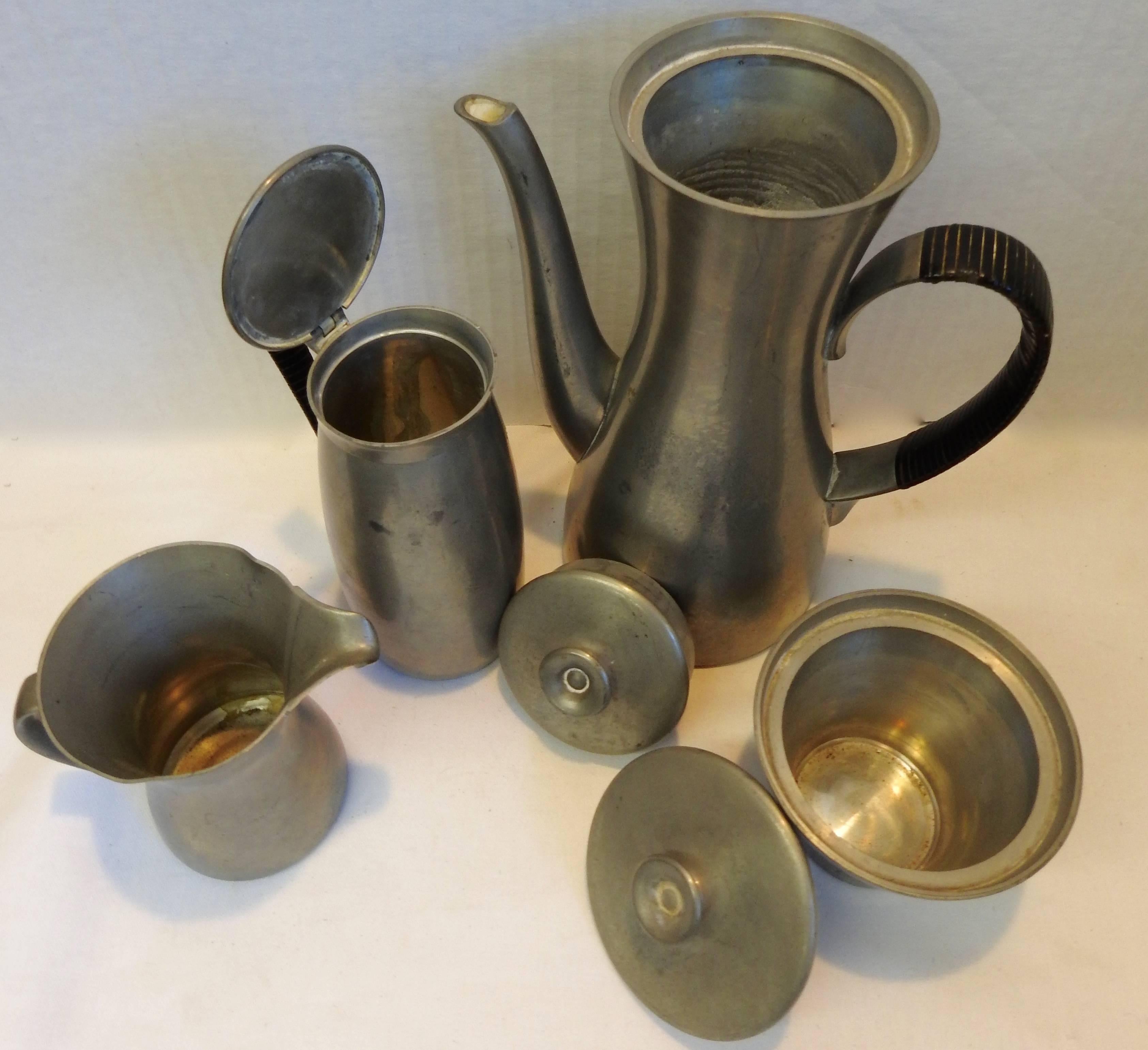 Royal Holland manufactured this midcentury tea or coffee set. It consists of a coffee or tea pot along with a sugar and creamer and a container for your waste of tea leaves or grounds. The handles of the two larger containers are wrapped in a black
