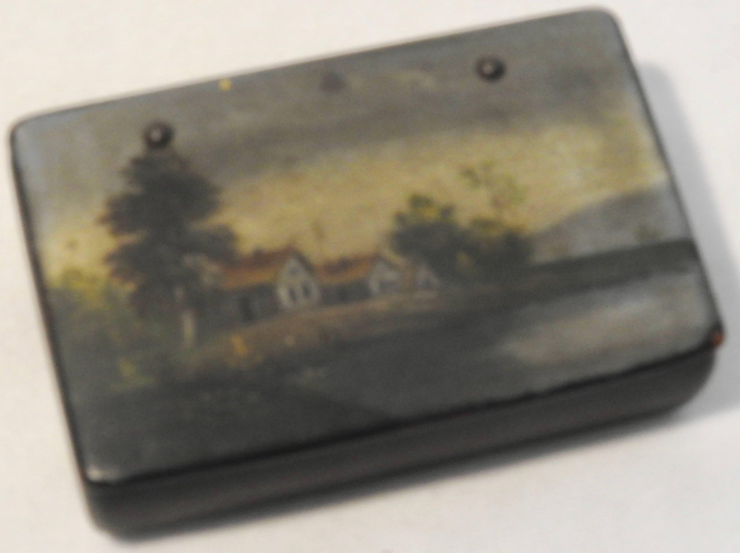 We are offering an antique black lacquer box from Russia with a hand painted landscape scene. It features a house along the banks of a river, surrounded by trees. The hinge is attached with brads.