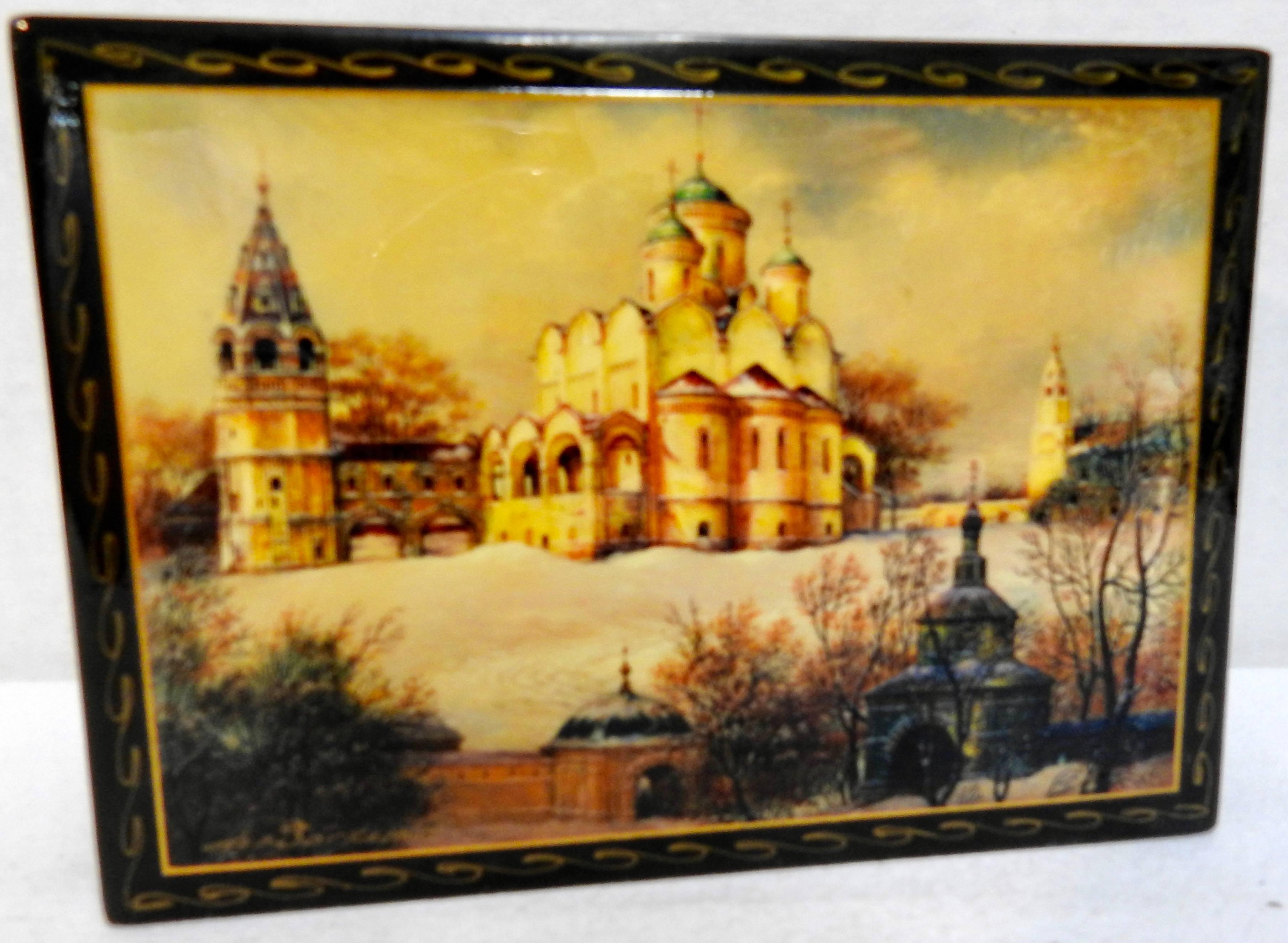 A snow scene surrounds the elaborate Annunciation Cathedral located near the Kremlin on this Russian black lacquer box. The edges are decorated in waves of gold and the top opens to a vibrant red. The top is signed but we could not identify the