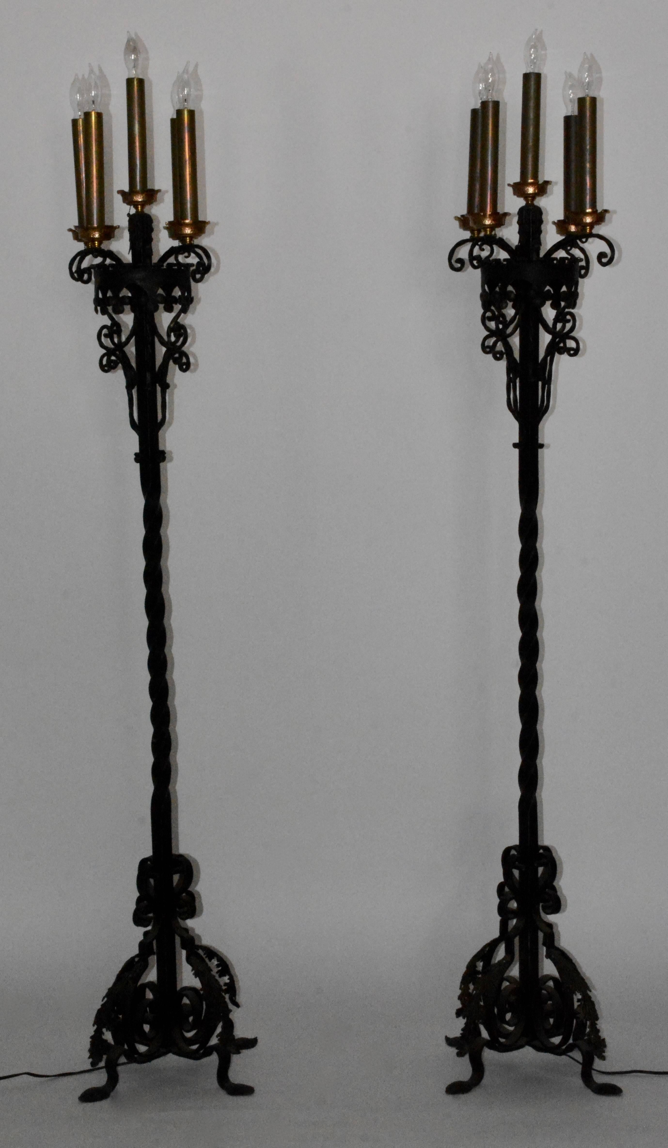 Features is a pair of 1920s Spanish revival wrought iron floor torchères. Each features gorgeous scrolling detailing. On top they feature five lights per lamp. Brass candle sleeves sit on top of beautiful copper bobeches. They both work and are