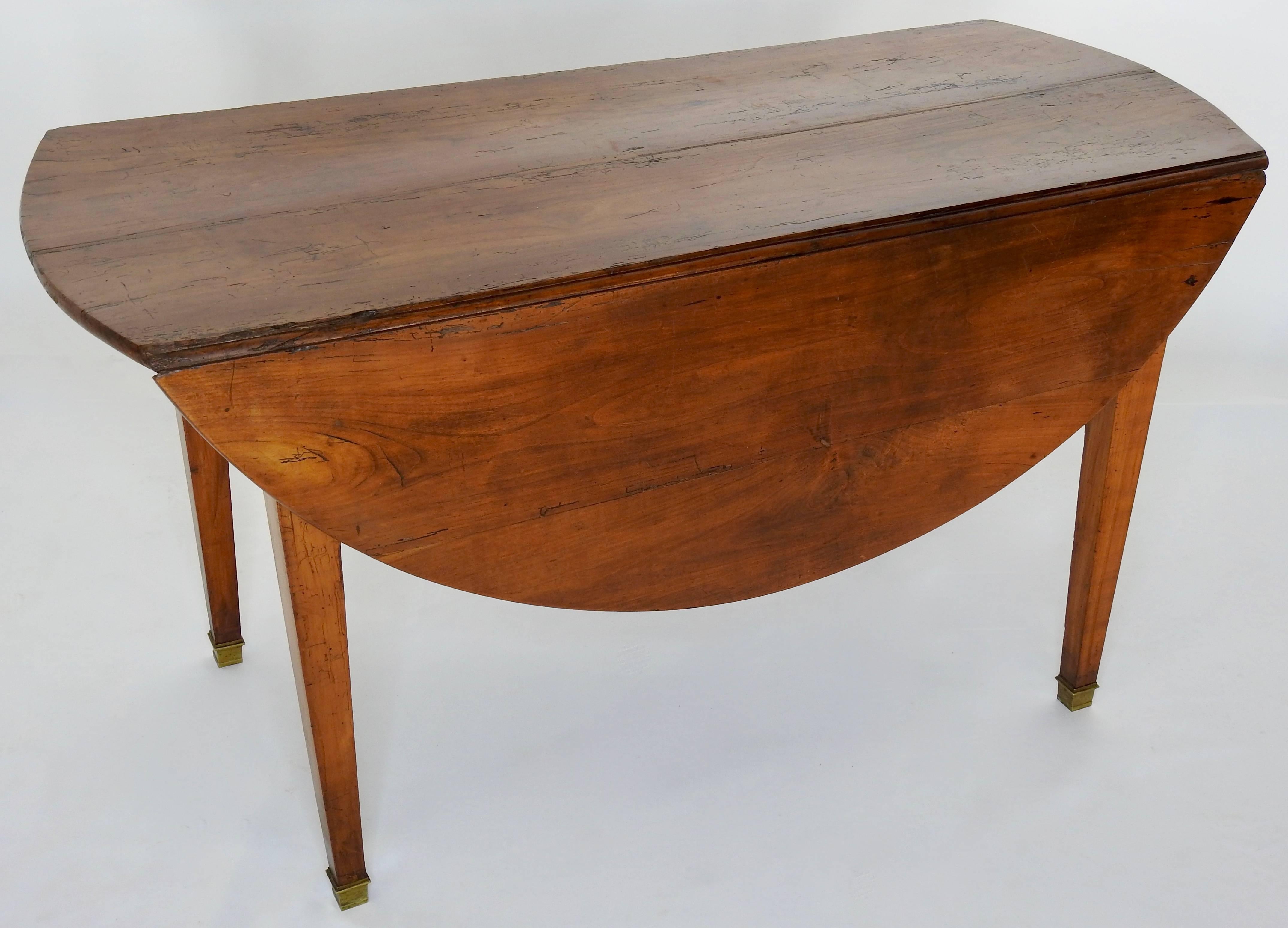 This is a classic drop-leaf table made of walnut from Italy. This warm toned table is a beauty. It sits atop square tapered legs that the ends are enveloped in brass with an aged patina. The top when let down is a narrow table with rounded ends and
