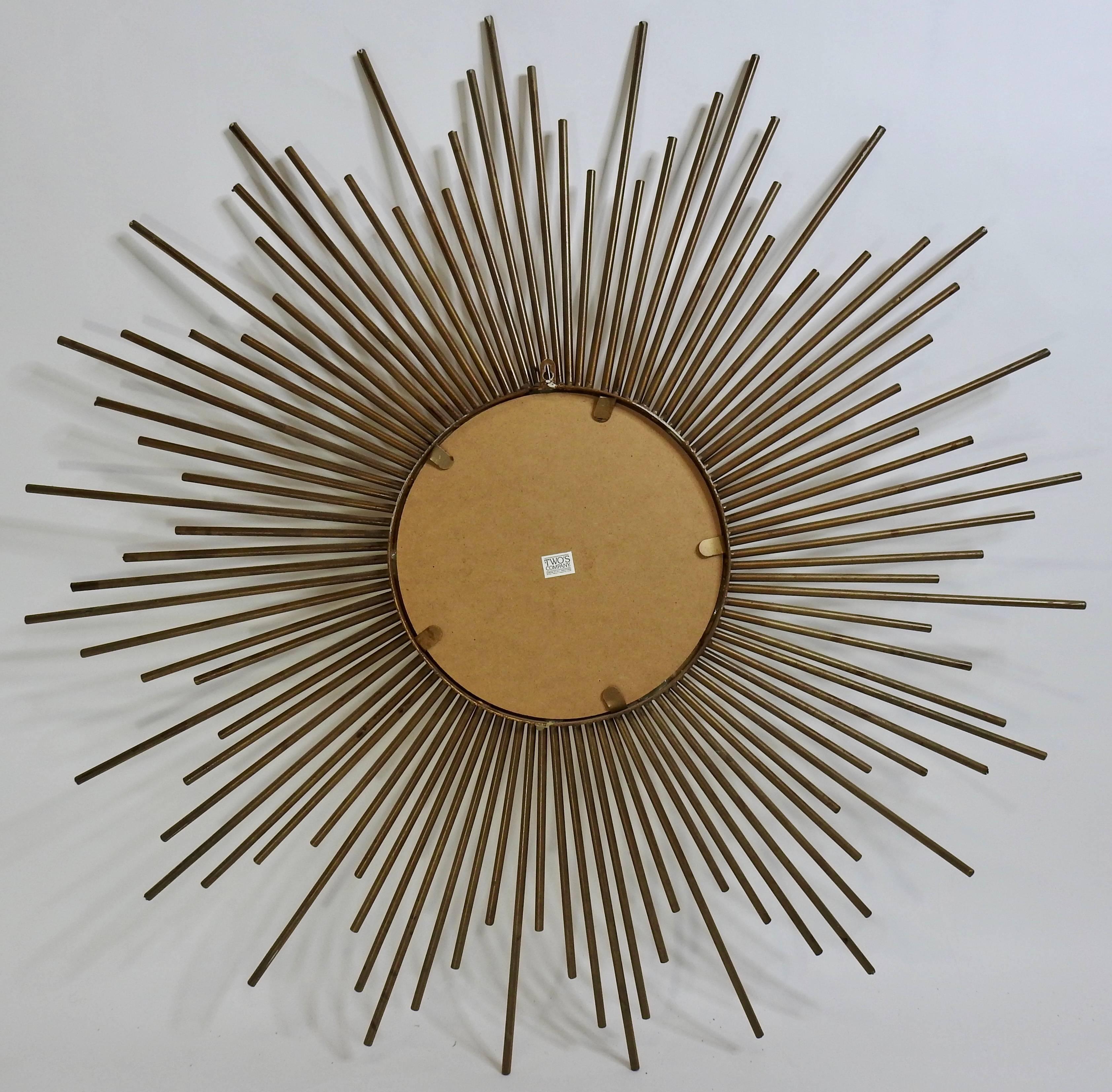 A vintage inspired starburst mirror. This mirror features a starburst frame, made of various length pieces of gold tone metal, with a round mirror in the centre. A “Two’s Company” sticker is on the back of the piece.