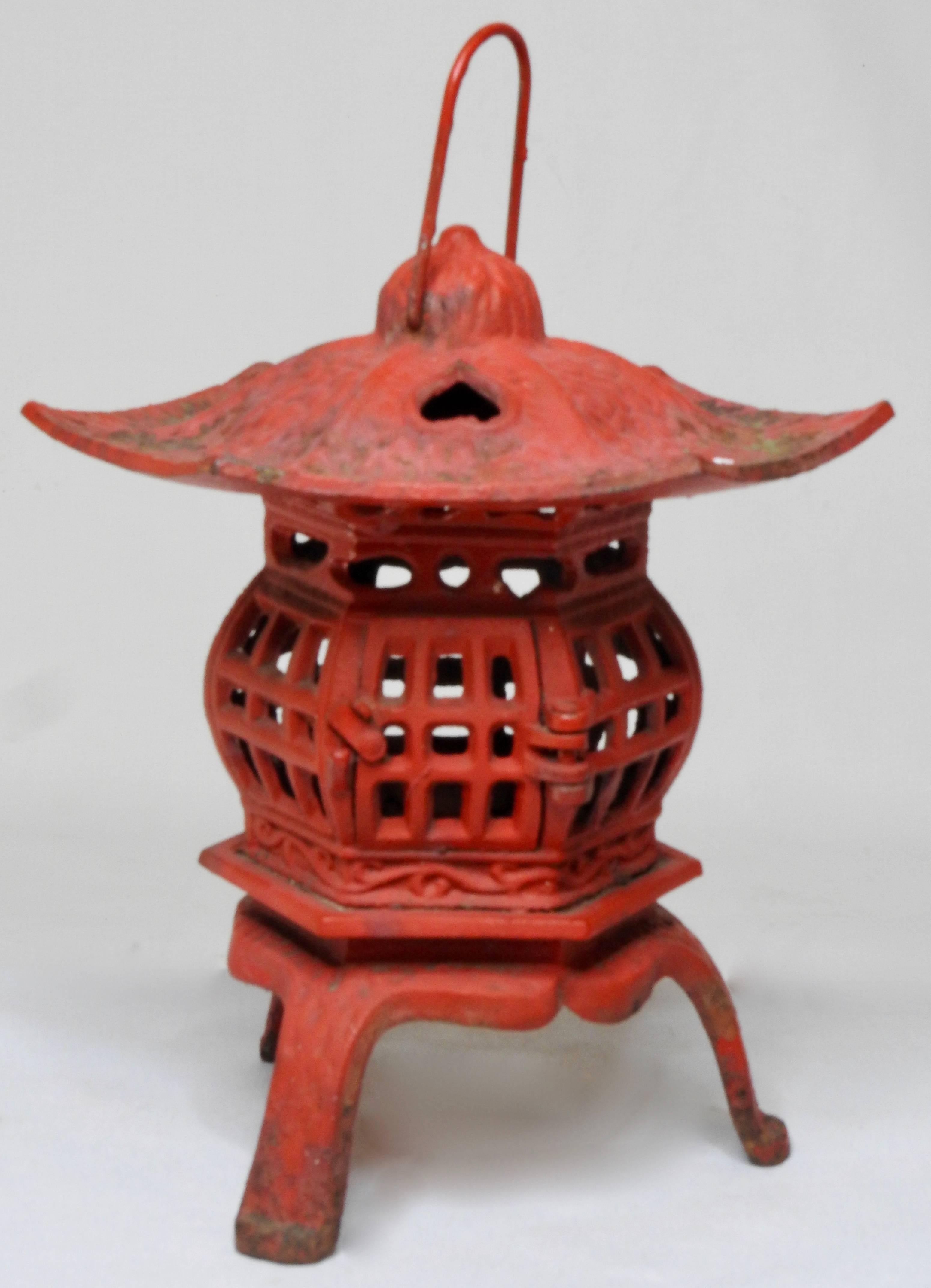 This vintage pagoda lamp is painted in a vibrant red color. It sits on three legs that with a curvy skirting. Has a hexagonal shape with open cut-out and an access door with latch and hinges. The top has a heart shaped cut-out and a hook for hanging.