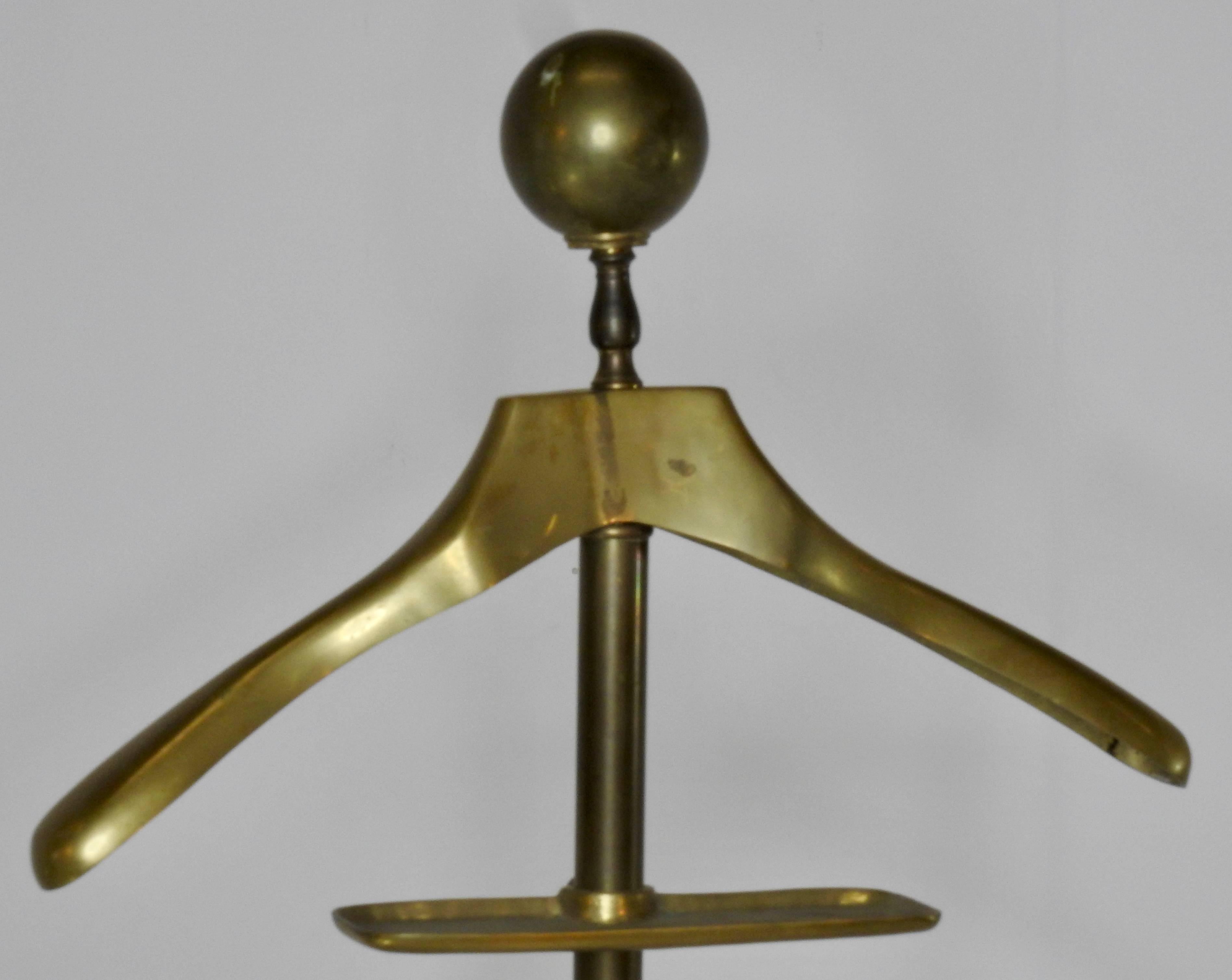 This is a solid brass valet by AITG and features unique twisted scroll legs. It has a hanger for your shirts and jackets as well as a bar for hanging your slacks. It includes a tray for your coins and accessories. Is marked solid brass and AITG INC.