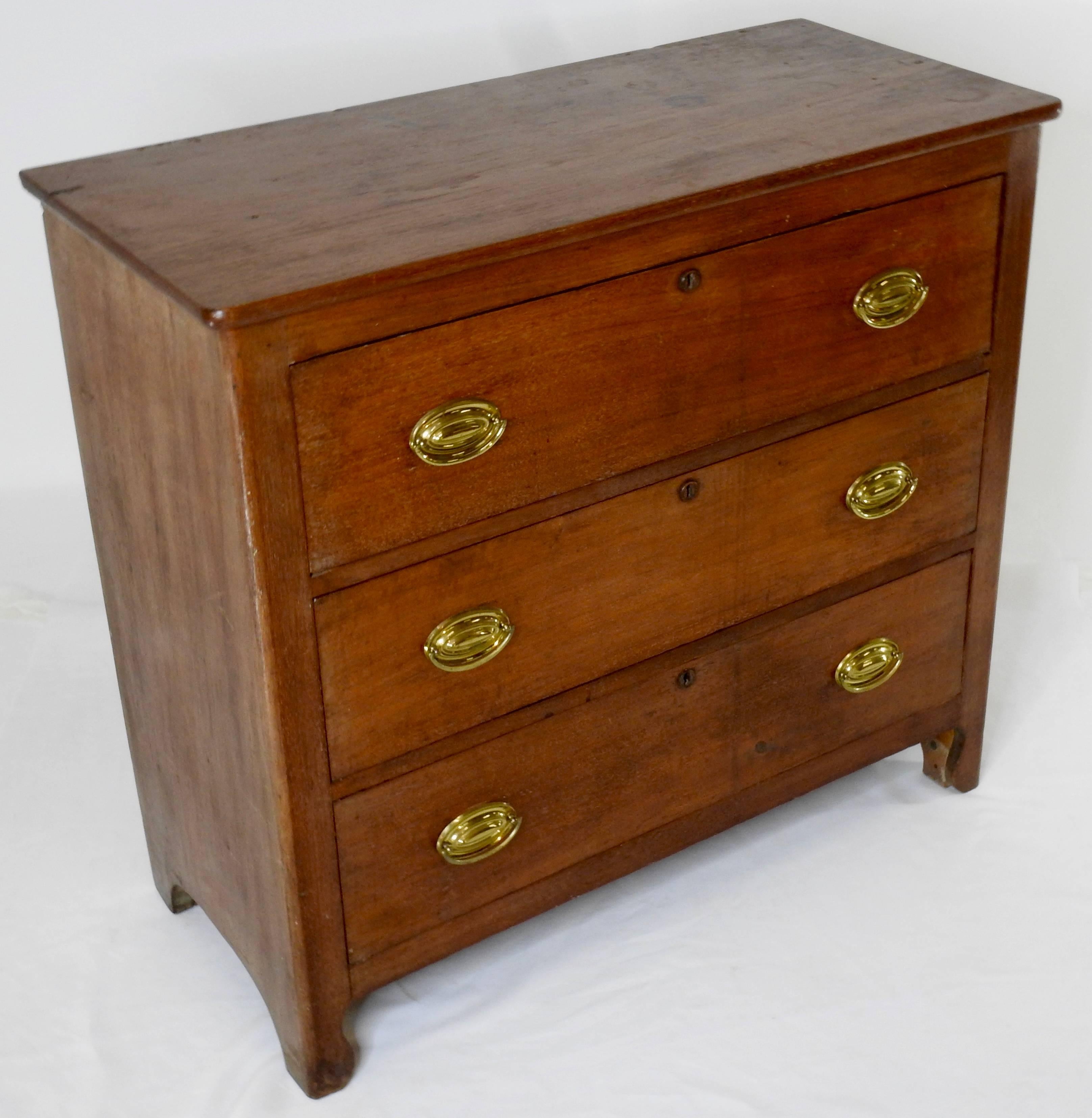 An antique Sheraton style cherry and mixed woods chest of drawers. The three drawers feature hand cut dove tails. The brass oval pulls are replacements. The case rests on simple curved feet that are extensions of the case frame.