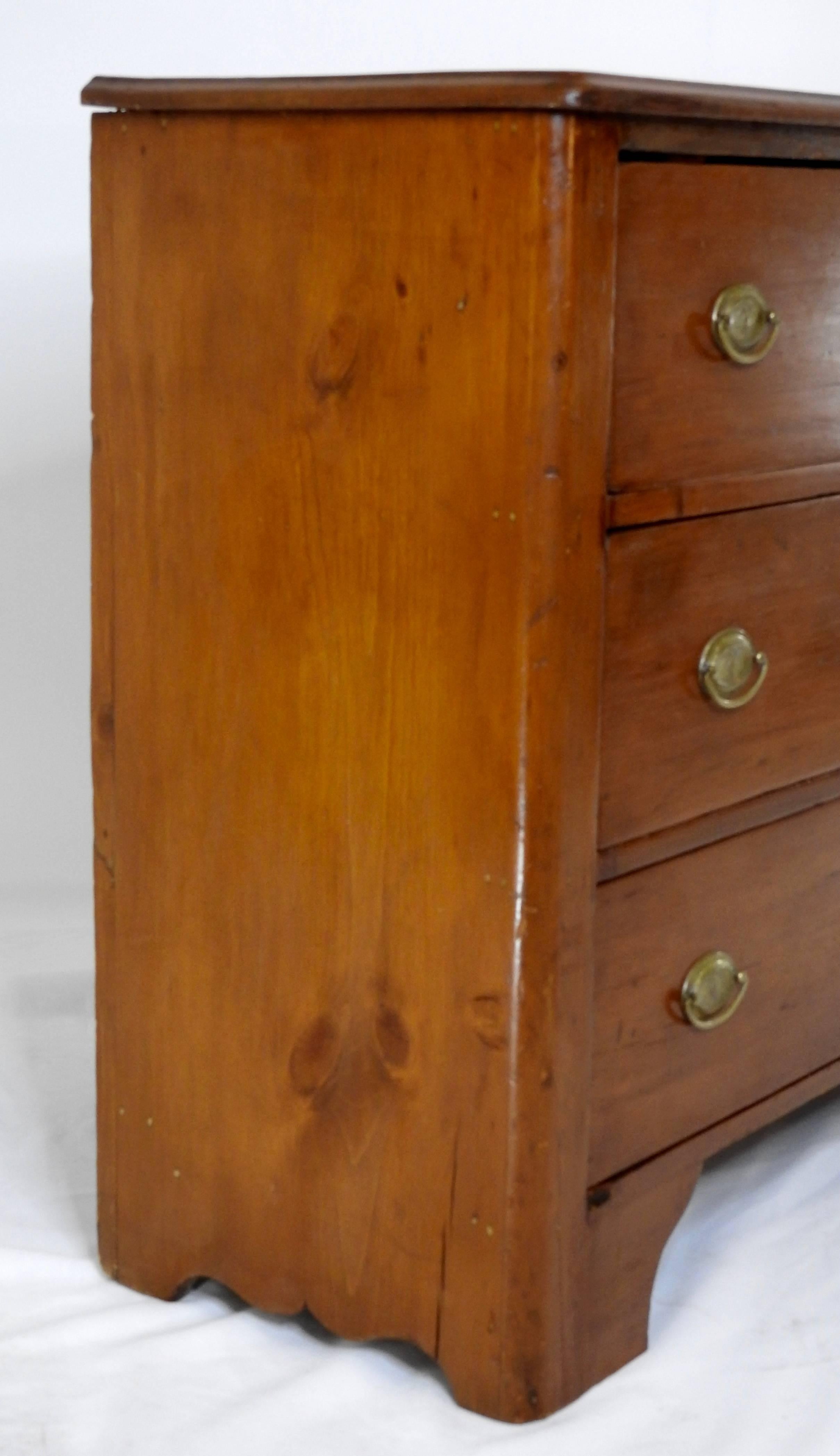 We are offering an antique American Federal style chest of drawers made in the 19th century. This cherry stained wooden chest of drawers features an overhanging edge top, three deep drawers with brass oval eagle motif pulls, keyhole accents and