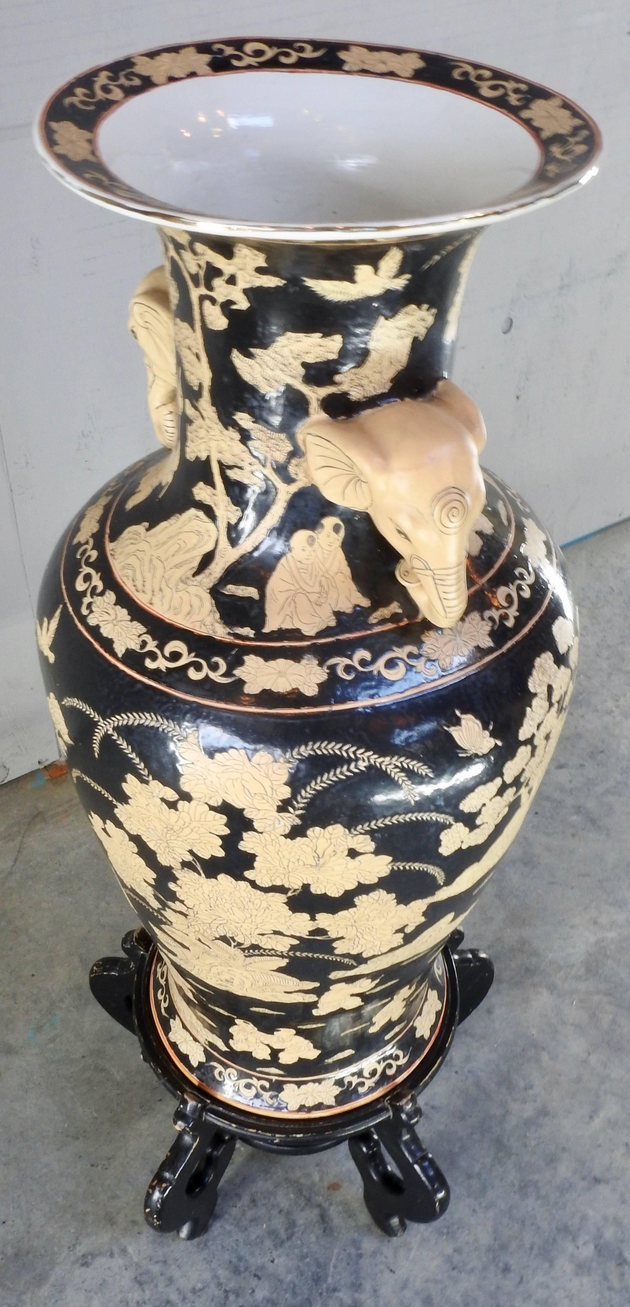 A pair of porcelain oriental urns accented with elephants for the handles. Black with ivory colored details featuring oriental scenes. The urns come with black lacquered stands.