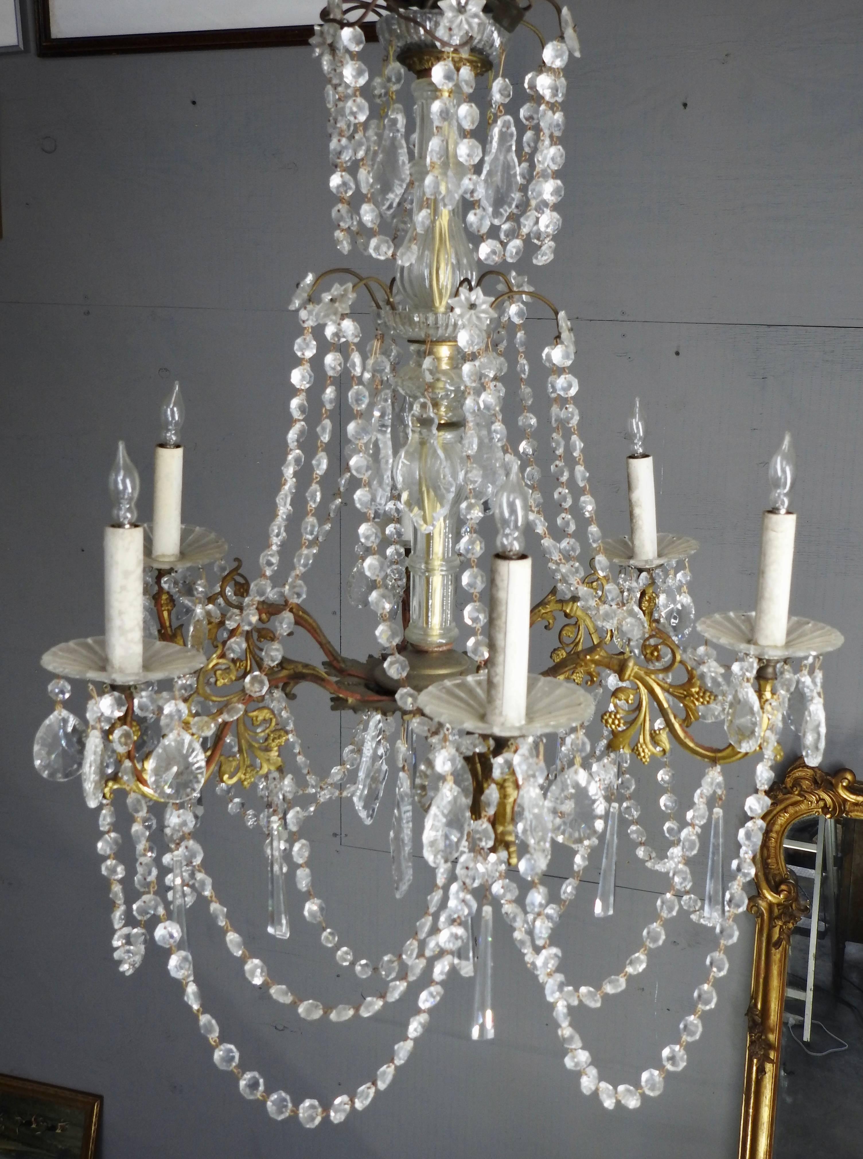 Strands of faceted crystal grace this elegant Country French chandelier. The light fixture is accented with many prisms and crystal bobesches. These are mounted on a bronze fixture featuring leaves and scrollwork. This chandelier was completely