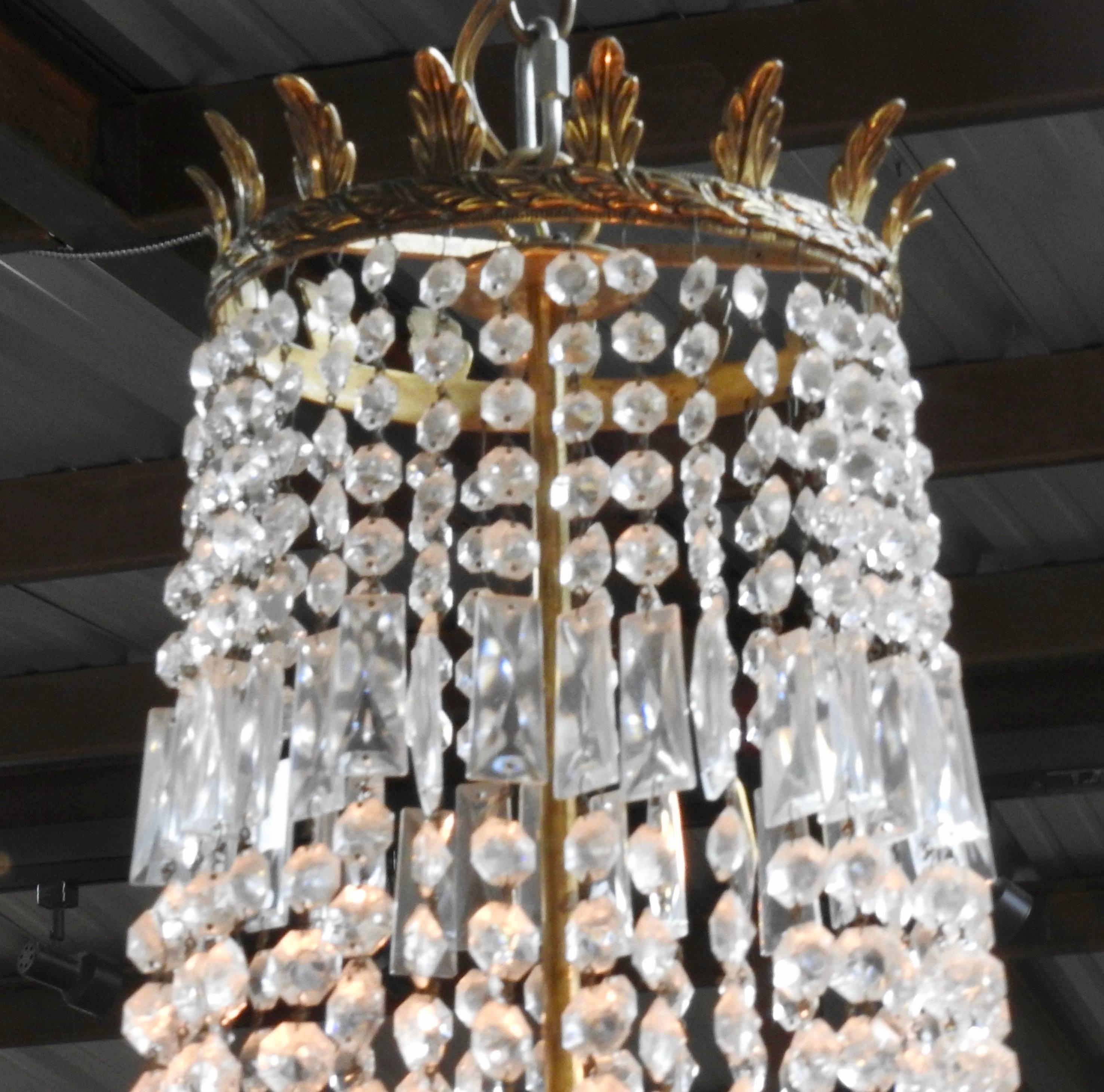 Stunning Empire chandelier from the early 20th century from France. Faceted crystal ropes with baguettes adorn the body of the fixture. Short plug drop crystals extend from the bobeches and the bottom cap. A crown with leaves tops off the crystals