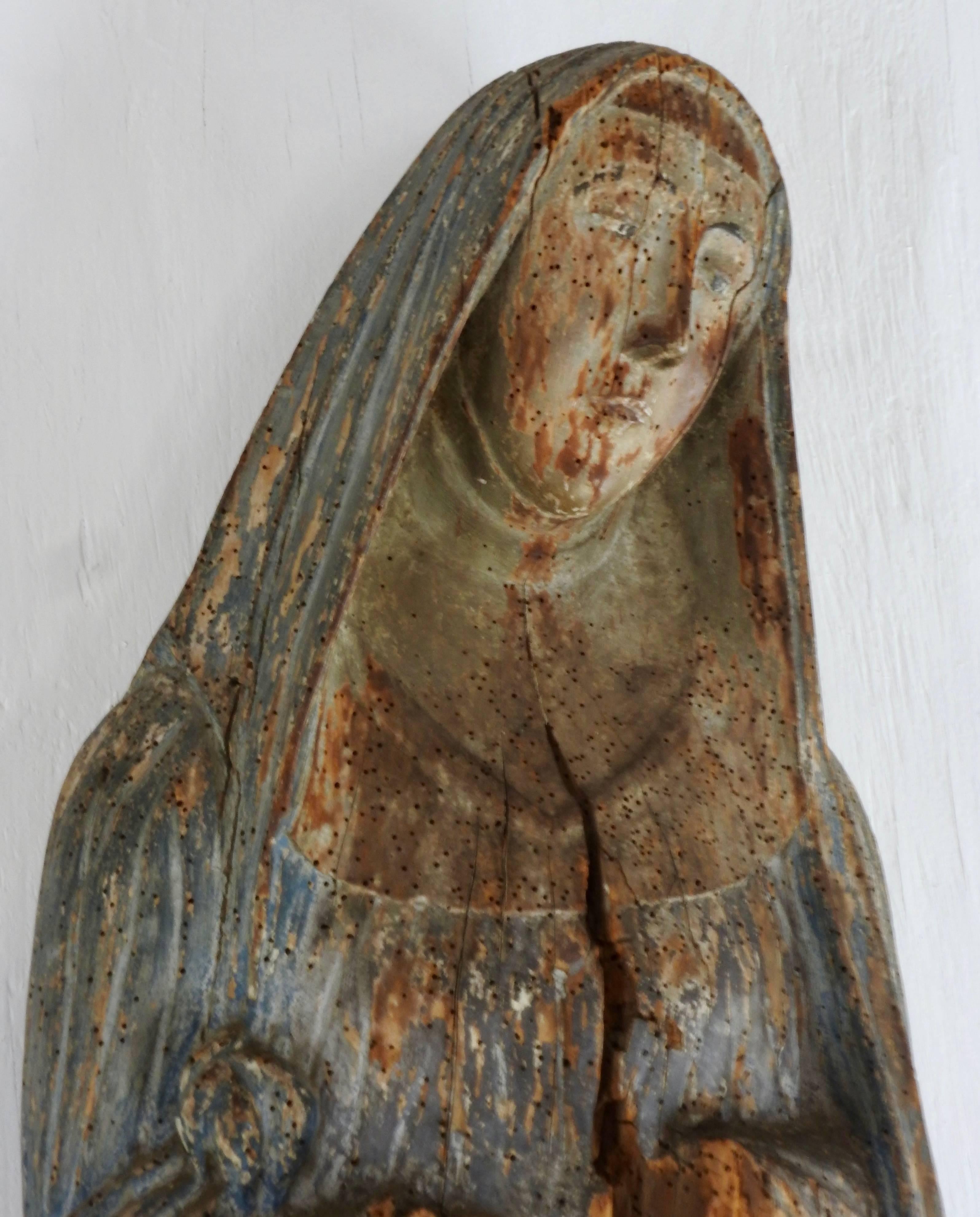 Primitive wood carving of the Virgin Mary from the early 17th century. The polychrome paint has softly faded over the years. There are some splits in the wood which is characteristic of the age of the piece. Her hands are missing. The back is open