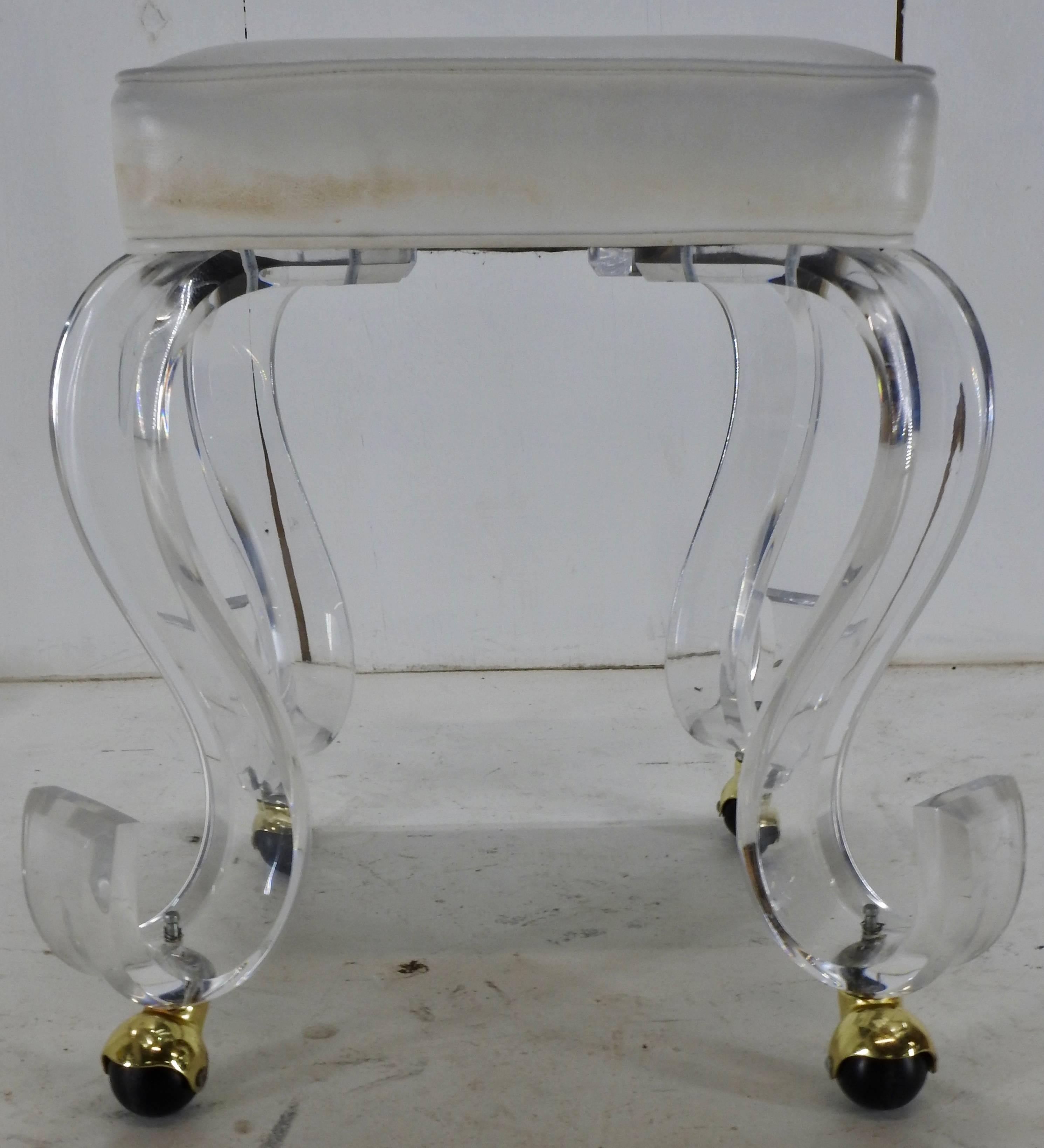 A modern era rolling stool on acrylic legs. The stool offers a white upholstered square seat set on ‘S’ shape acrylic legs with gold tone caster feet. A maker’s mark was not found on this piece.