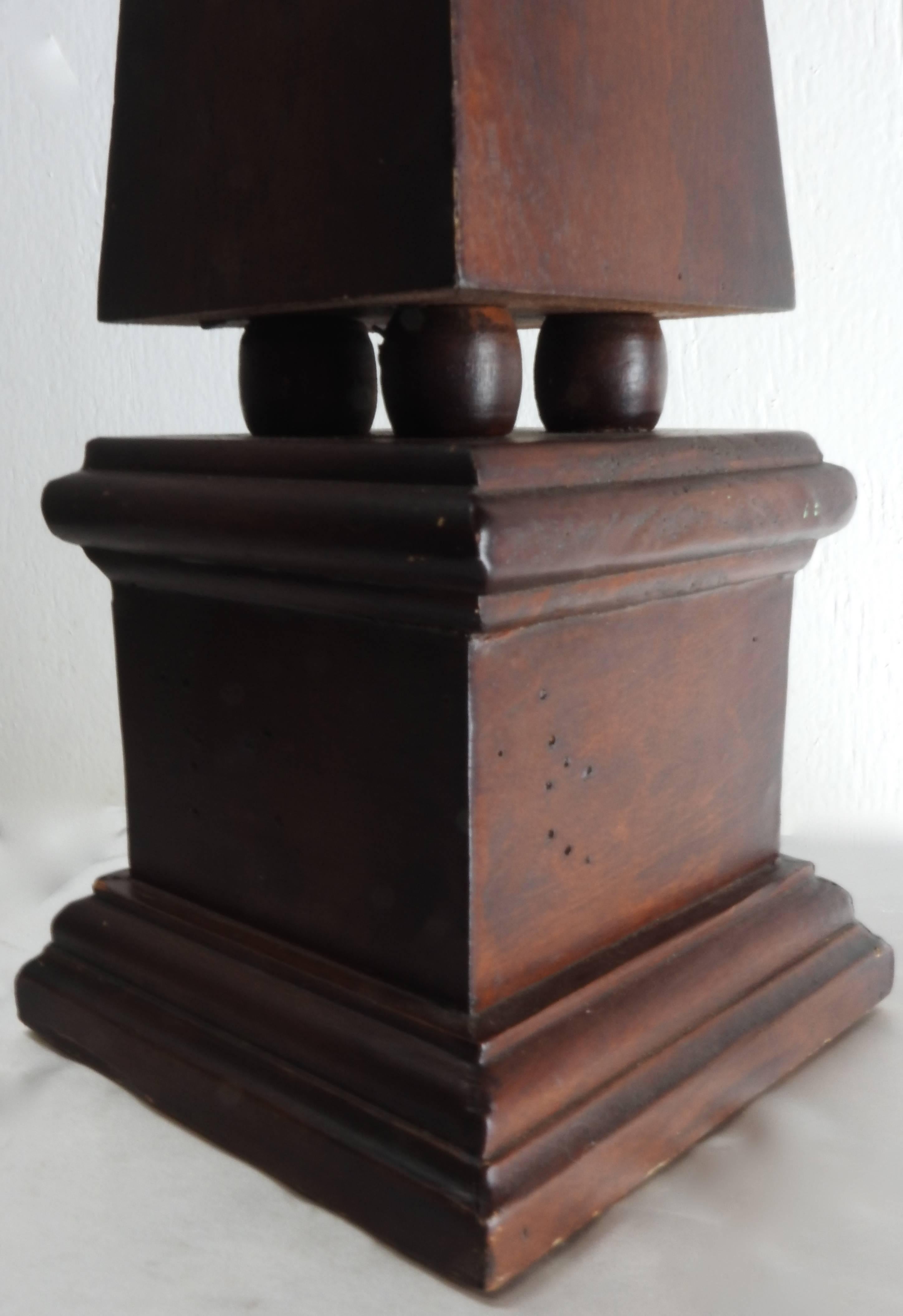 This is a vintage walnut obelisk dotted with worm holes. This tabletop piece features a square base and has four non-scratch foam pad circles on each bottom corner. The piece is not marked.