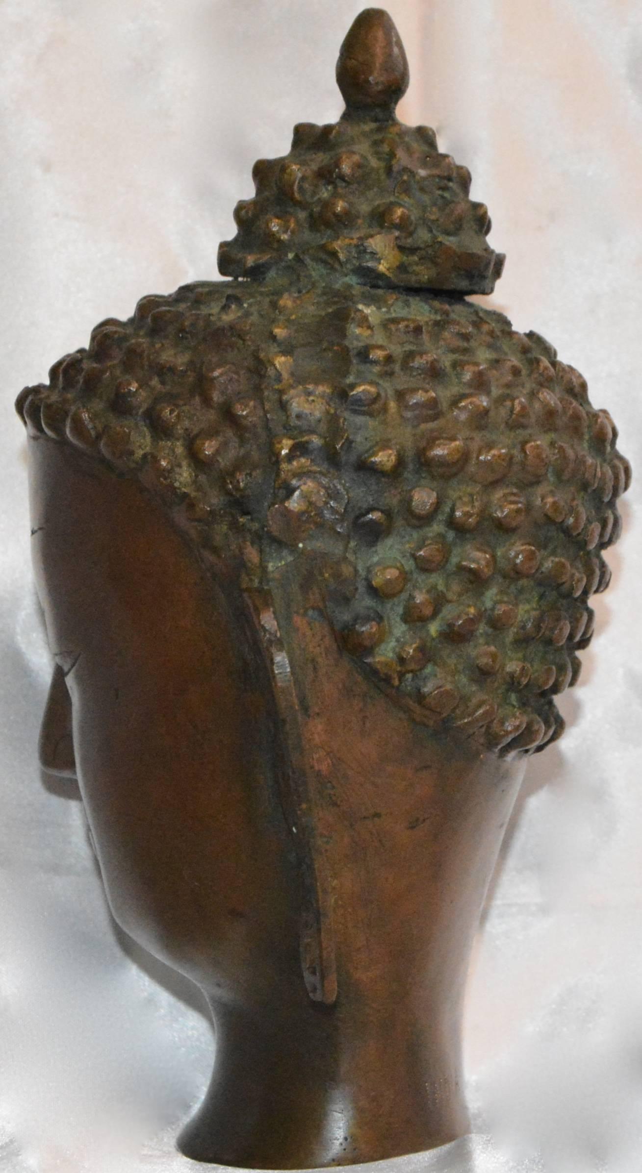 This is a stunning Thai bronze head figurine. It depicts a Buddha with elongated ears, tight curls and the ushnisha on top of its head. No visible maker’s marks. It is stamped India on the back.