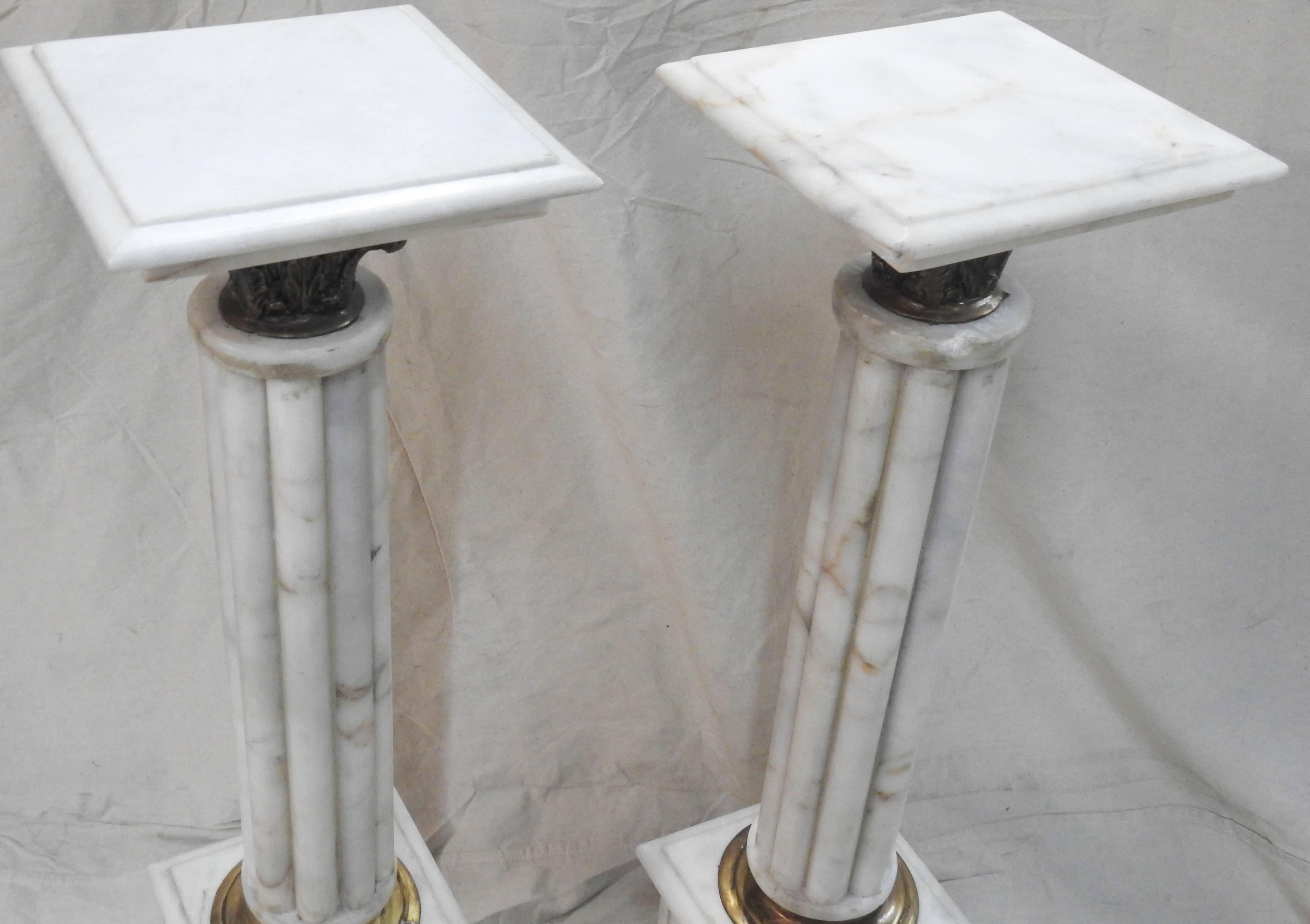 Featured is an elegant pair of Carrara marble pedestals in shades of white with grey. The square top will be a perfect place to display your prized possessions or a trailing plant. They are enhanced with cast bronze details.
