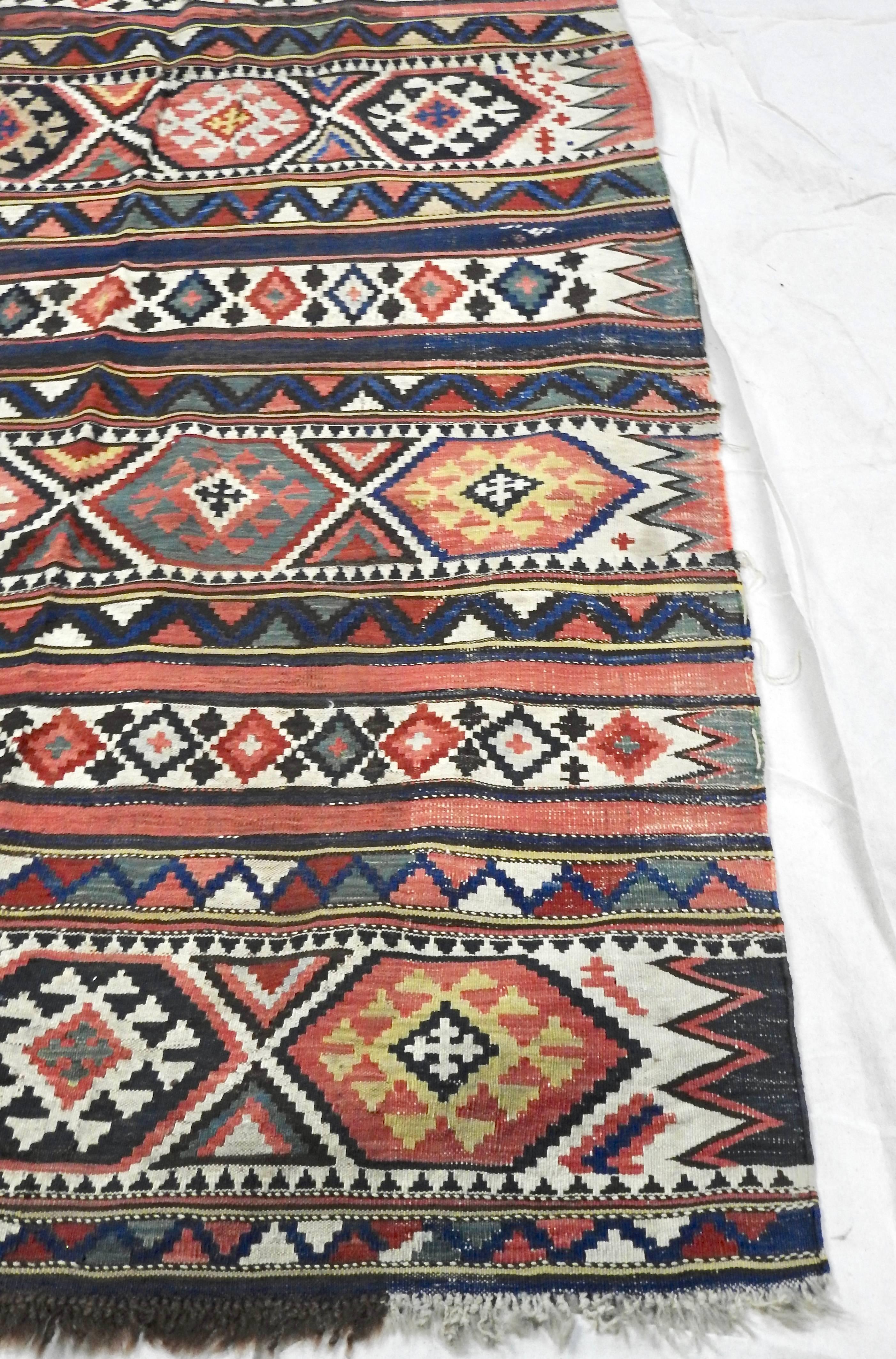 This is a lovely handwoven Turkish Kilim carpet runner. This rug features stripes of horizontal panels of scorpion, running water, and eye motifs in a palette of dark blues, greens, reds, pinks, yellows, and browns. It has a hand-tied, natural,
