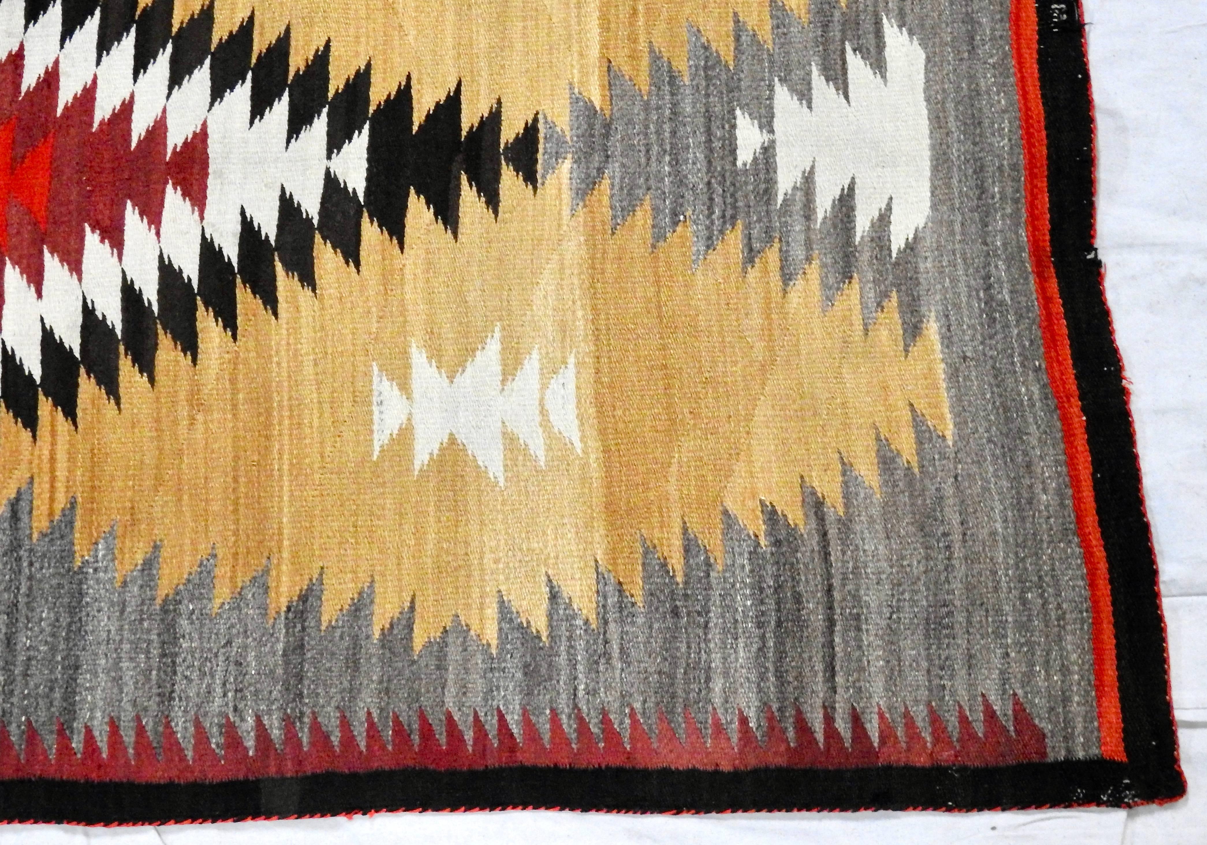 Featured is a classic, circa 1940s regional Navajo reservation eye dazzler rug. The rug is hand loomed in gold, gray, red, black and ivory wool. The pattern displays a large, elongated diamond at the centre with half diamonds at each end with red