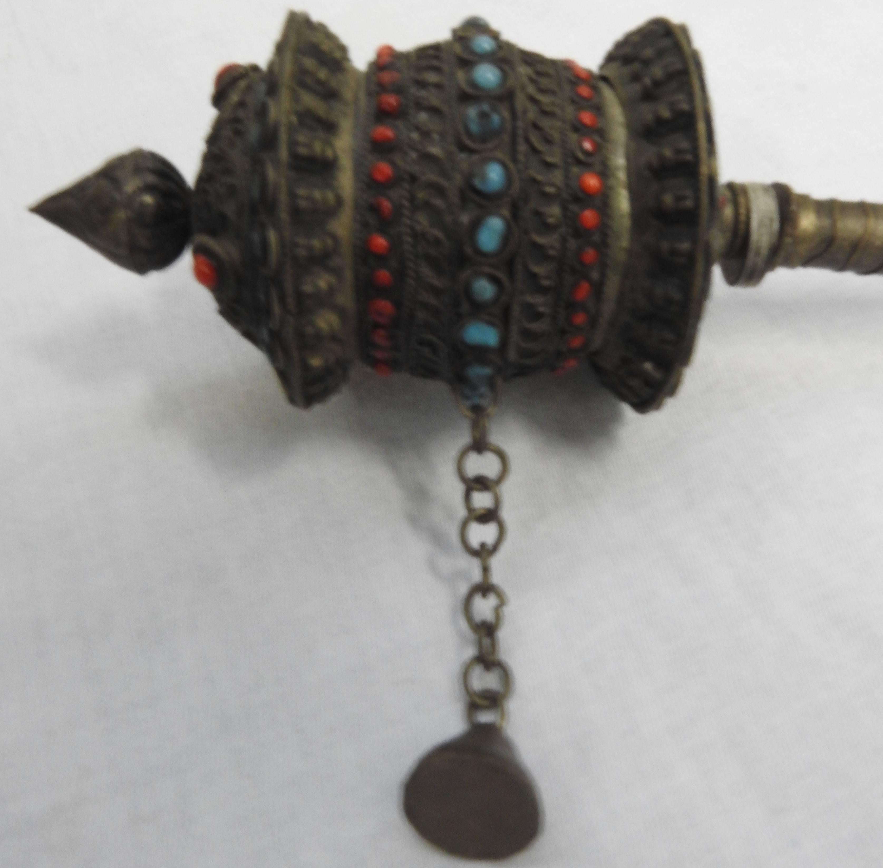 This is a Buddhist Mani prayer wheel. This silver hand-held Mani consists of a tapered handle on a central spoke, around which revolves a cylindrical mill head etched and decorated with multicolored stones. The mill head opens to reveal a thin paper