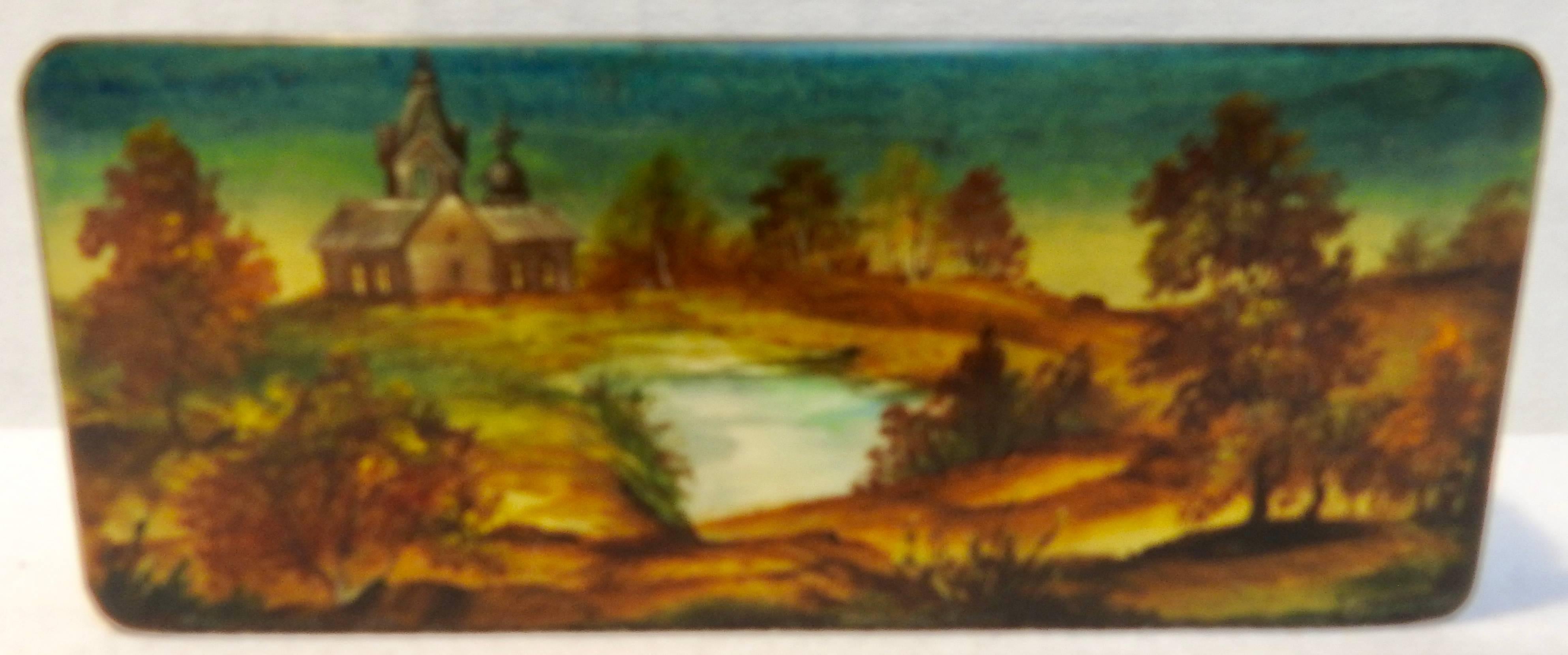 We are offering a small Russian black lacquer box that has been hand painted. The mother of pearl river scene is surrounded by rolling hills with trees and a fabulous building in the background. The warm colors on the lid are beautiful. The lid