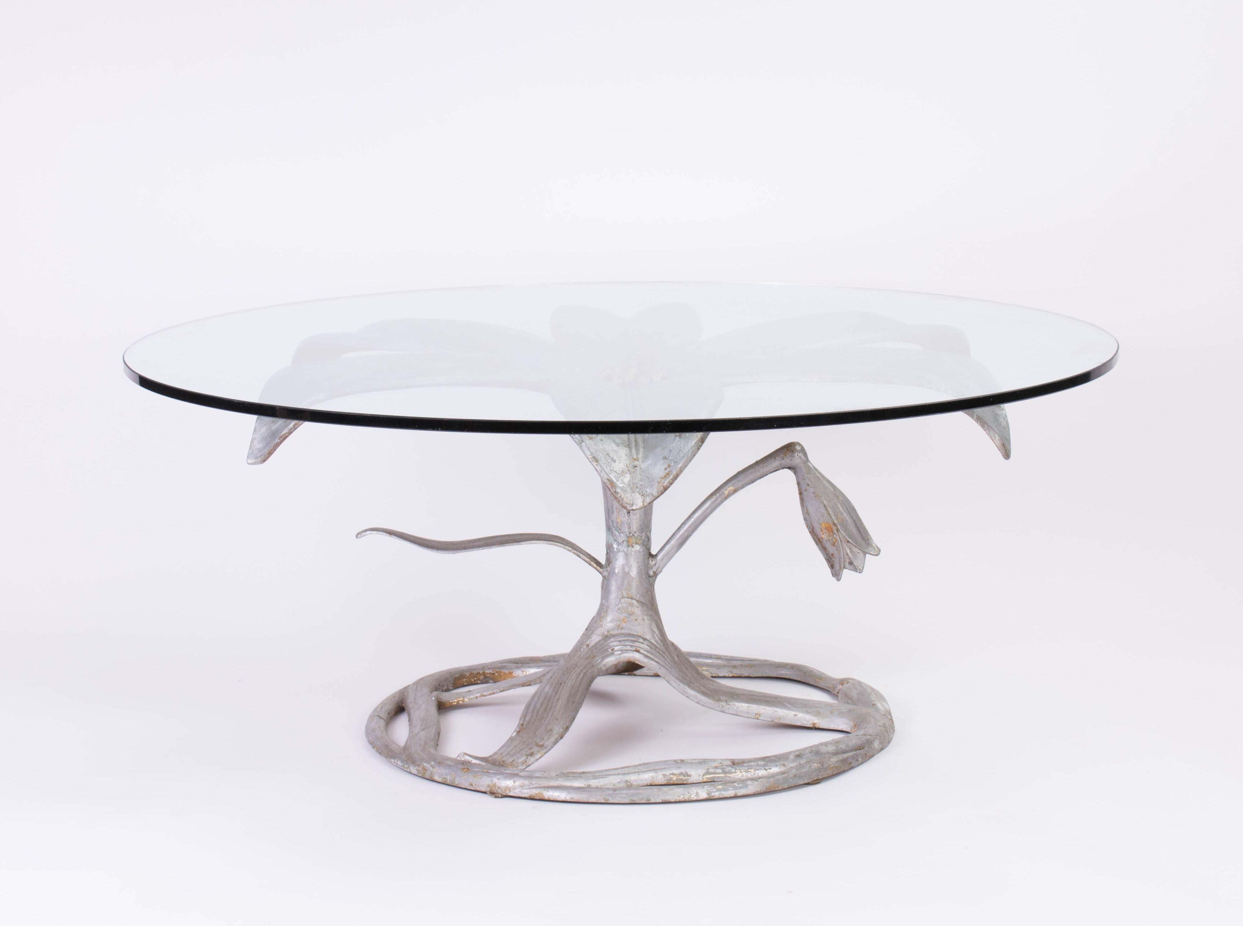 Arthur Court coffee table in the shape of a lily. 
The material is aluminium with small fragments of gold color. It has a circular glass top with two minimal chips.