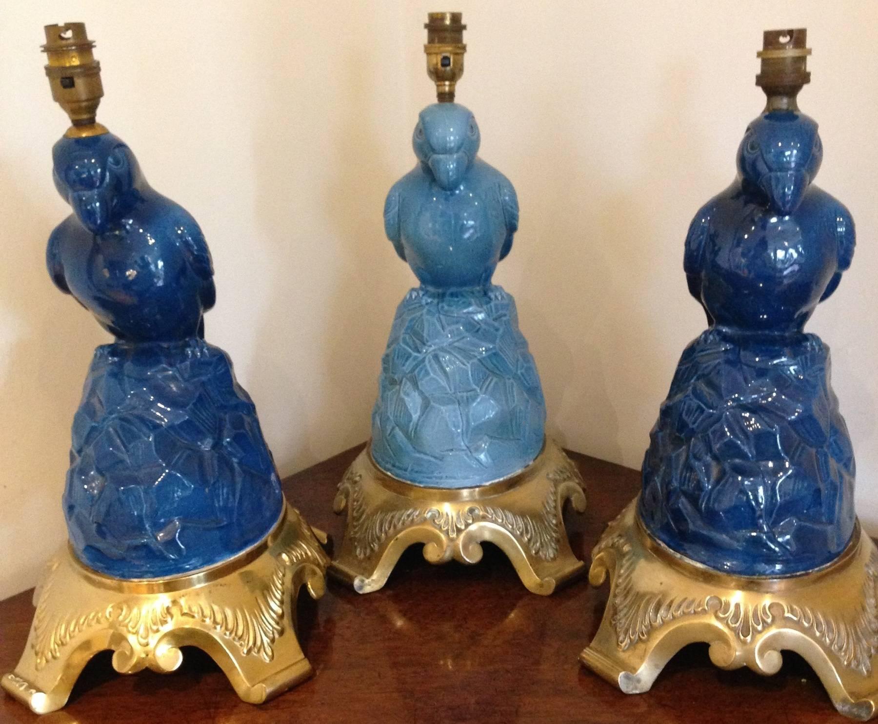 A set of three blue(two matching, one lighter) glazed porcelain lamps in the form of stylized parrots, resting on fine. Cast heavy gilded bronze mounts. No visible signs of factory marks.
