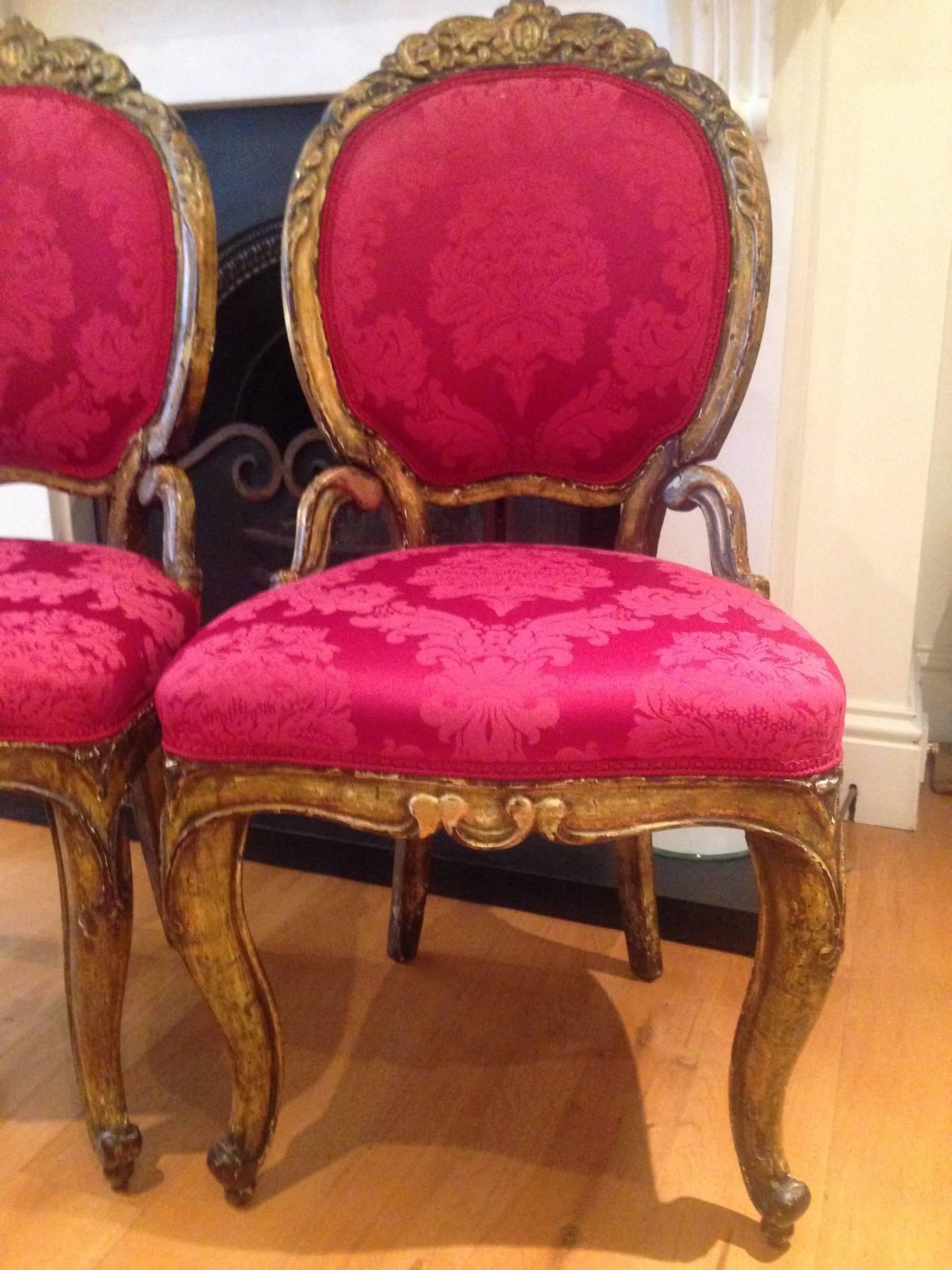 A pair of pretty partial gilt Italian 18th century side chairs, reupholstered in deep red and pink damask. The chairs have undergone restoration at some point and are still in need of a little more work on them. Some of the gesso has chipped off and