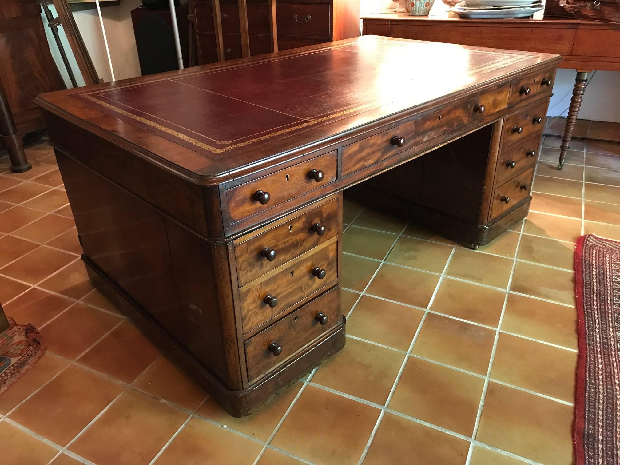 An impressive double sided partners desk with dark red tooled leather top over three drawers to either side, supported on a pair of pedestals with drawers to one side and panelled cupboards to the reverse. The desk is made in three sections in