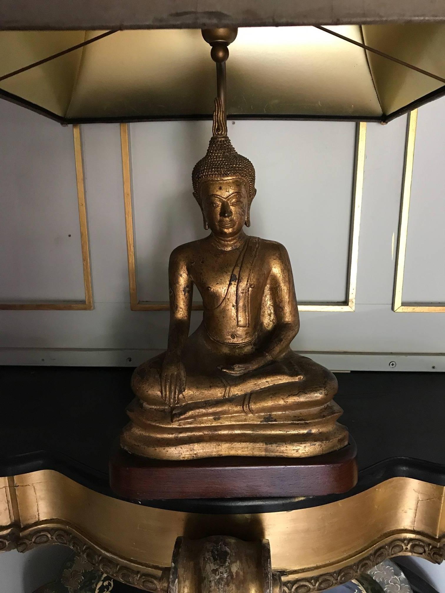 A stunning gilded metal Buddha lamp on a heavy wooden base. Shown here with its original silk shade. The shade has some water marks and wear to the braiding, so could be changed or recovered, though works perfectly well as it is.
