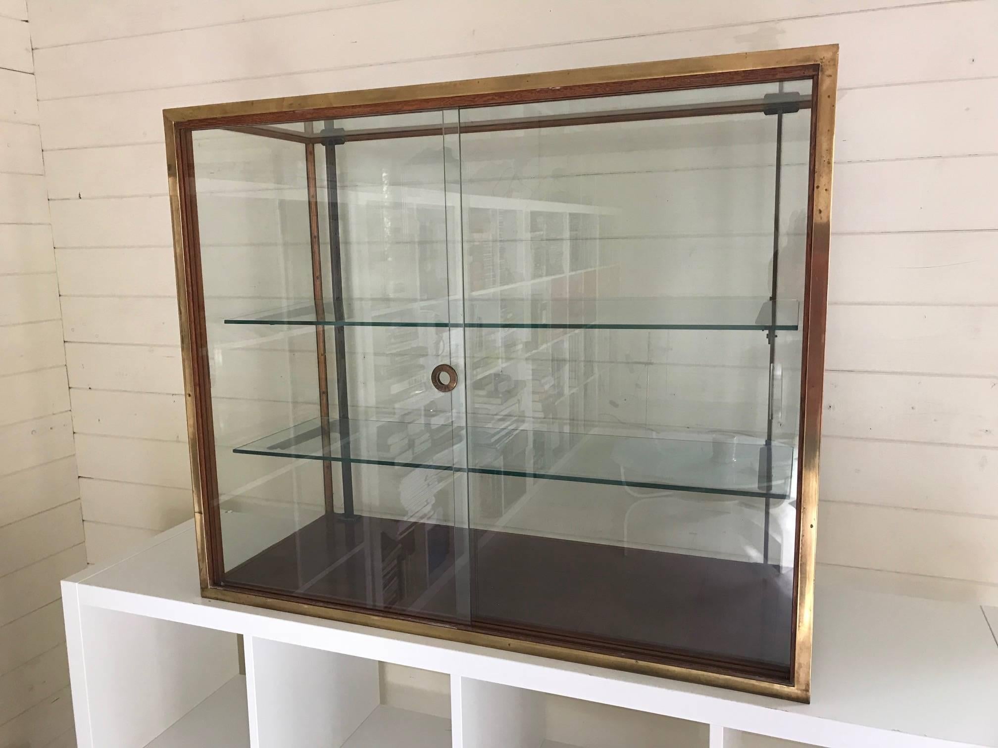 A great quality brass, wood and glass vtrine. Two sliding doors and shelves. Patent mark to the sliding integrated door handle. Shelves and doors are removable for transport. There are some chips to the glass shelves and corners of the doors. If the