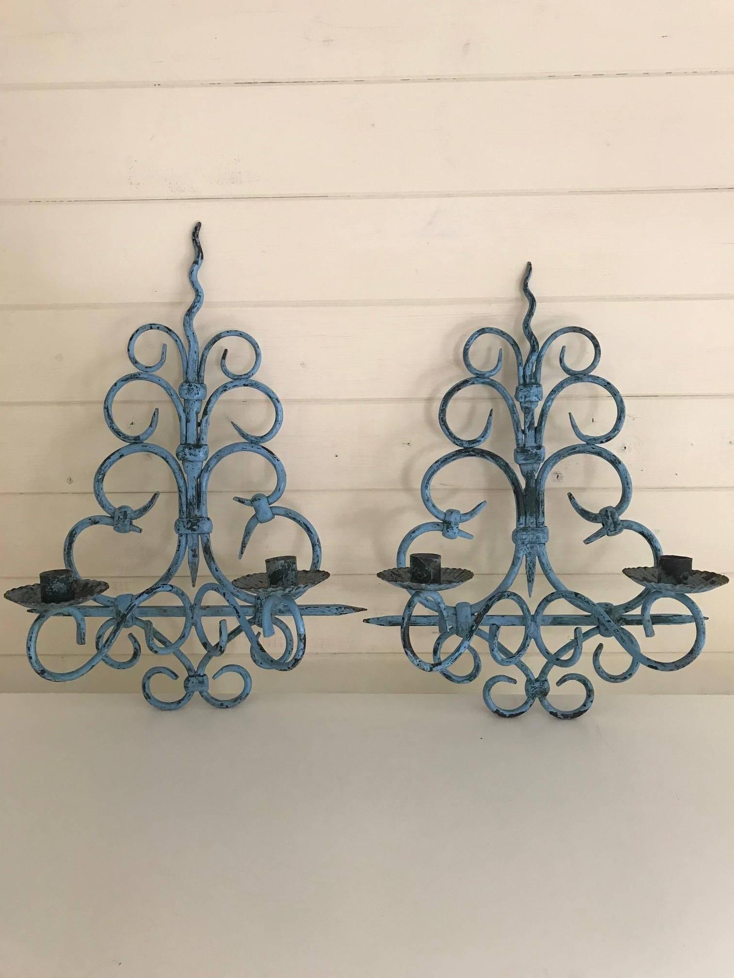 A matched pair of French solid wrought painted iron wall light sconces. Traces of green and blue paint showing. Can be used currently with candles or rewired to be used with electrical fittlings. One of the lights is slightly taller than the other.