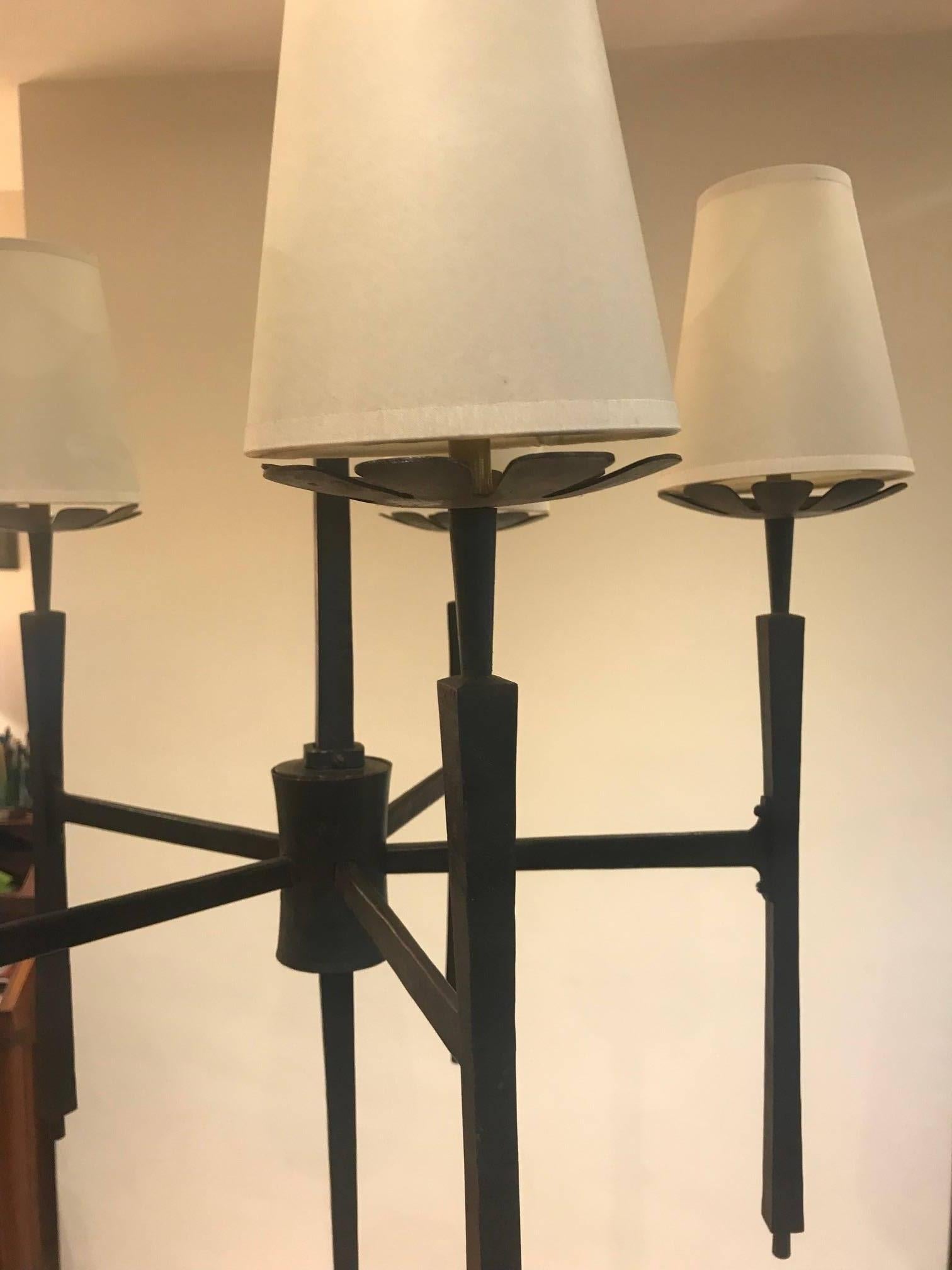 A very long wrought iron five-armed chandelier with interesting detail to the lamp holders and finial. Five card shades, one of which is slightly damaged.