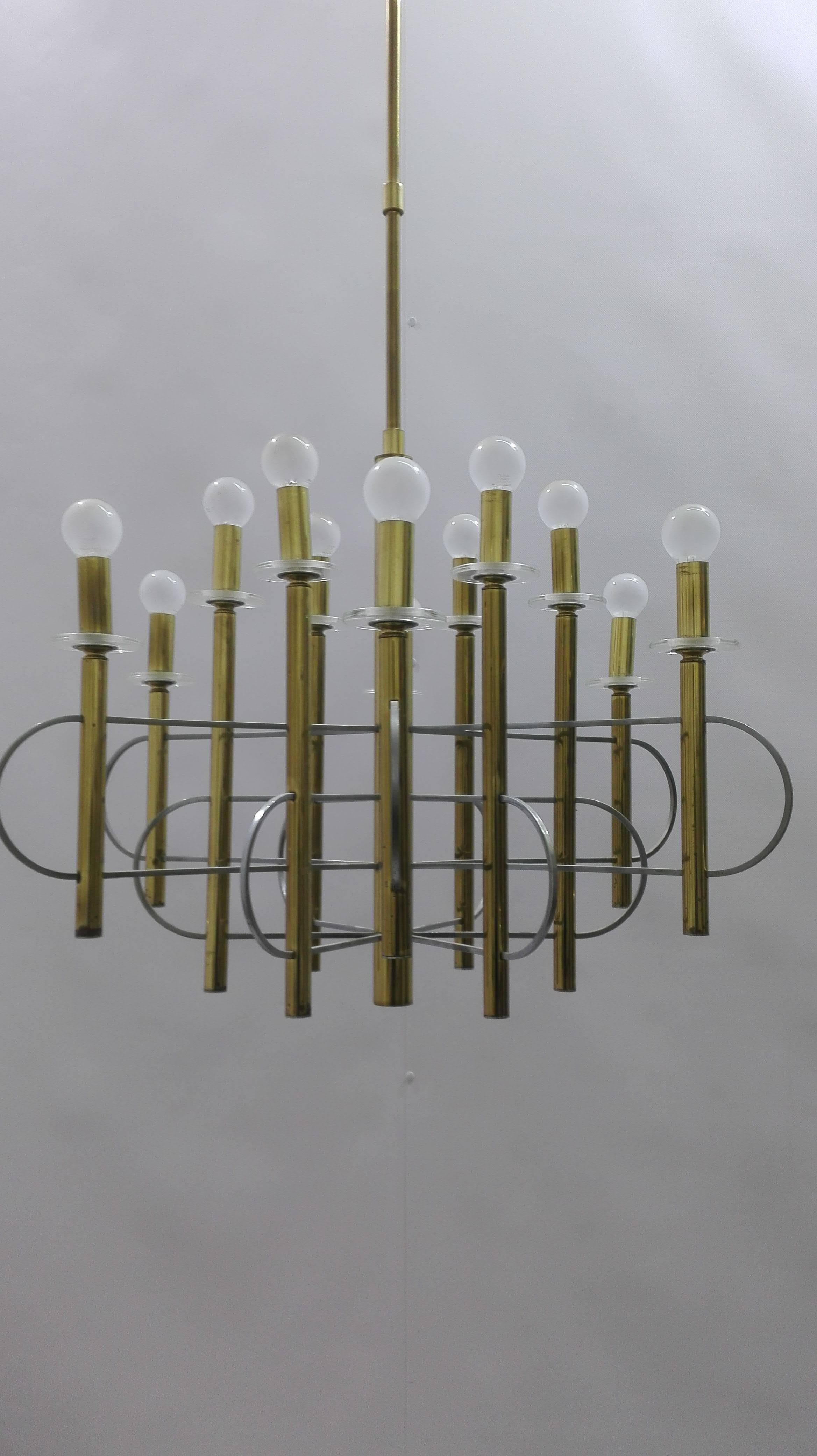 A brass, chrome and glass twelve-light chandelier by Gaetano Sciolari (1927-1994), the twelve two-tiered lights with a circular glass drip pan supporting a brass sleeve, interlaced together around the central brass them by chrome atom-like spokes.