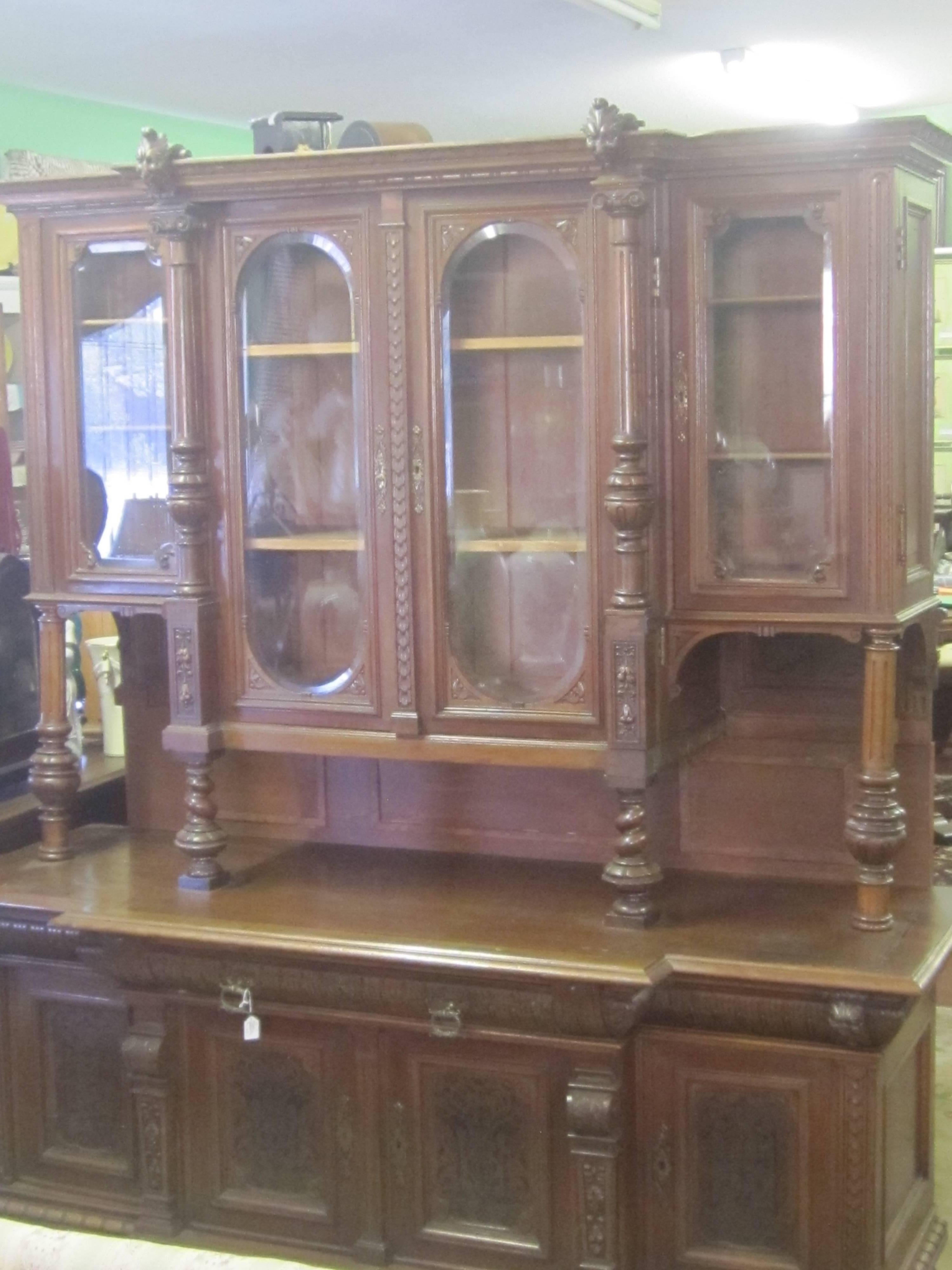 This beautiful 19th century breakfront is walnut with carved face motif details at the top. There are burled columns and burled details and the glass panes are bevelled. This piece has been in a private collection and handed down through the family