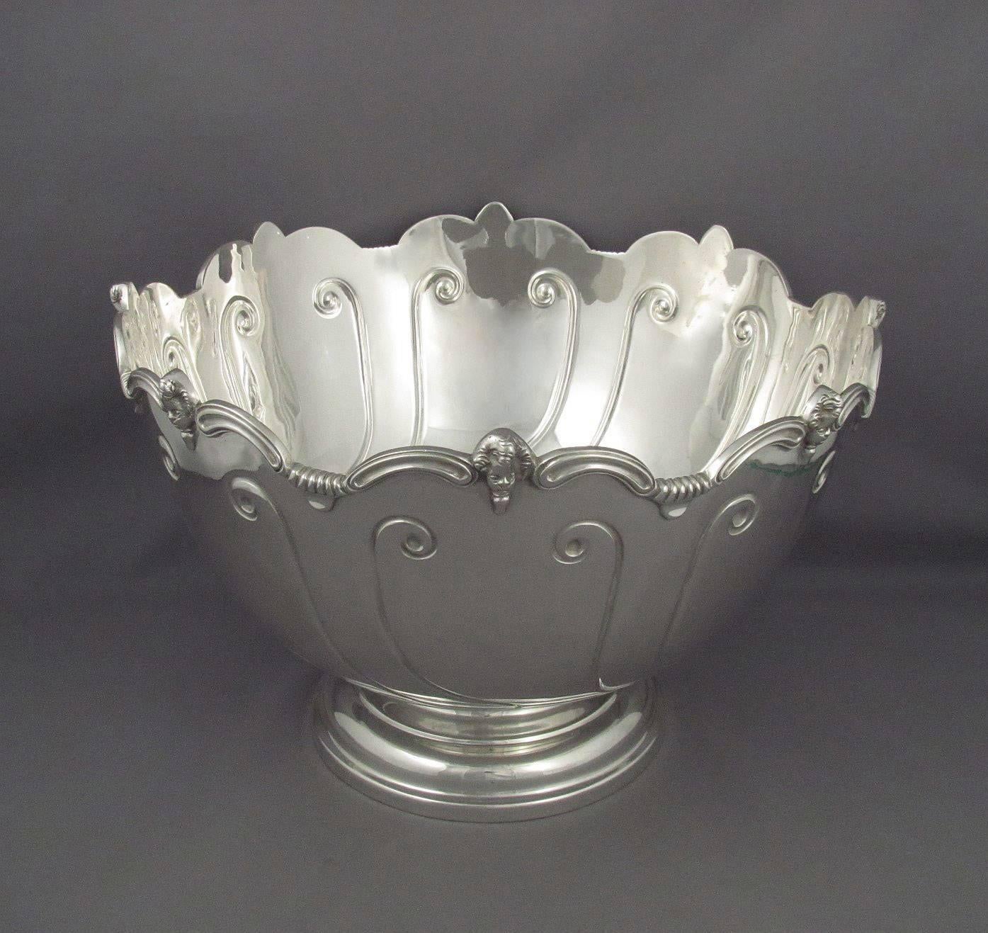 An antique silver Monteith style punch bowl by Thomas Bradbury & Sons, hallmarked Sheffield 1910. Scroll edged rim with cherub masks, the body embossed with scroll, on pedestal foot. Measures: 12.25" (31.1cm) diameter, 8.25" (21cm)