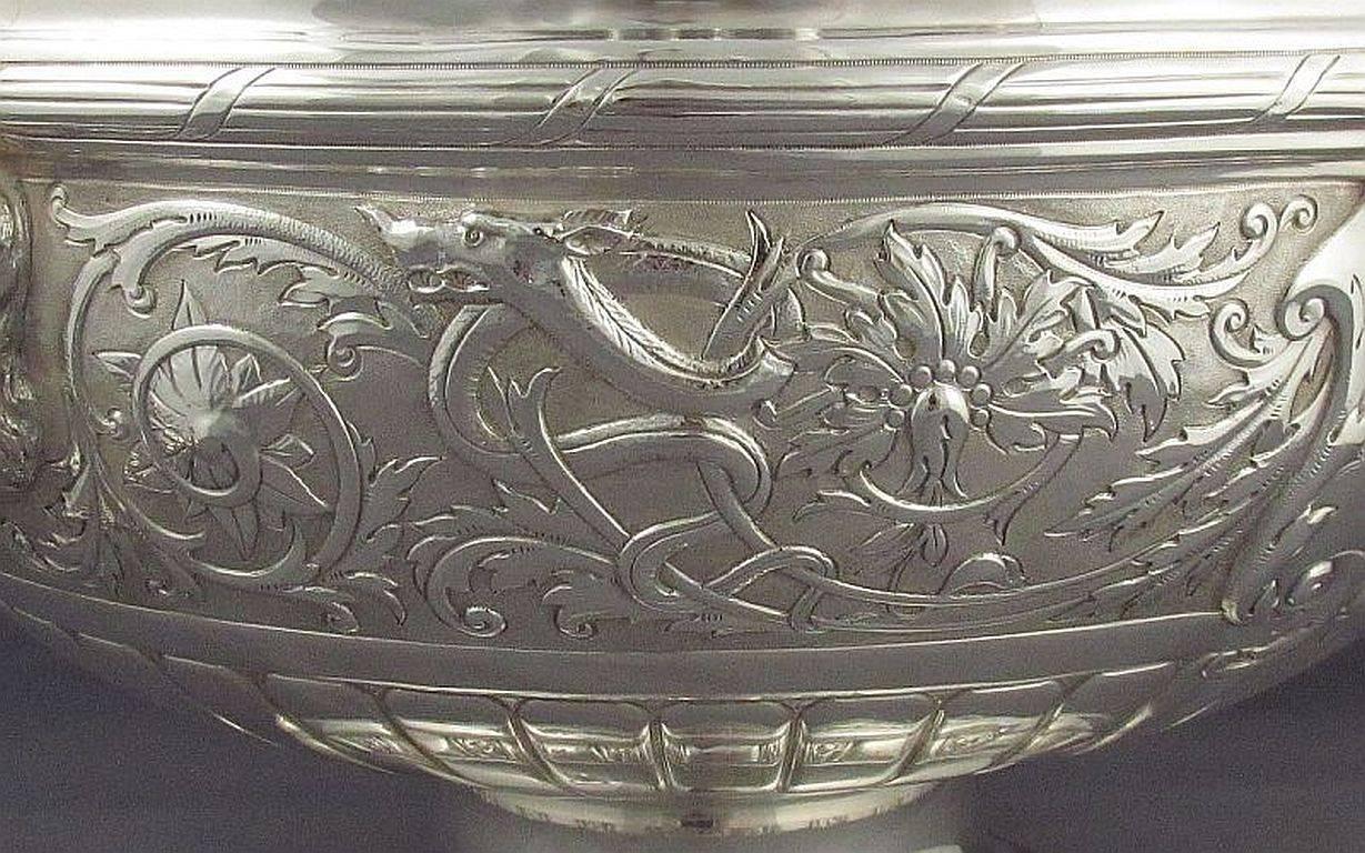 A beautiful Edwardian sterling silver Monteith style punch bowl by John Round, hallmarked Sheffield 1901, with retail mark of Warings London. Embossed with masks, foliage, dragons and wreaths, with lion's mask and ring handles, on pedestal foot.