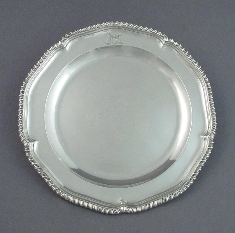 A pair of early George III silver dinner plates by renowned silversmith Thomas Heming, hallmarked London 1763. Circular with shaped edge and gadroon border. Engraved with a family crest. 9.5