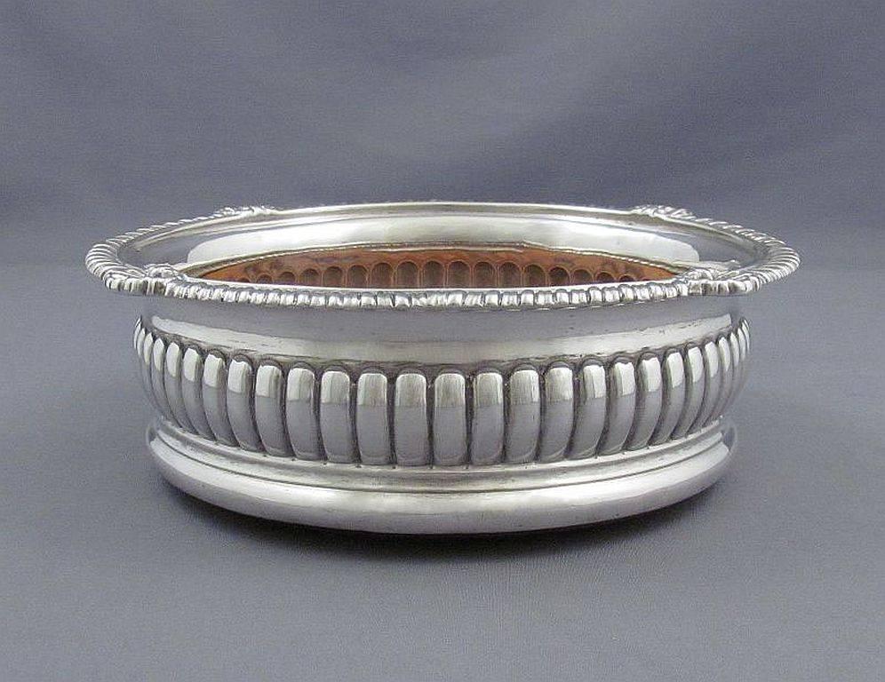 A handsome George III sterling silver wine coaster by William Bennet, hallmarked, London, 1809. Fluted convex sides and applied shell and gadroon border with turned mahogany base. Measures: 6