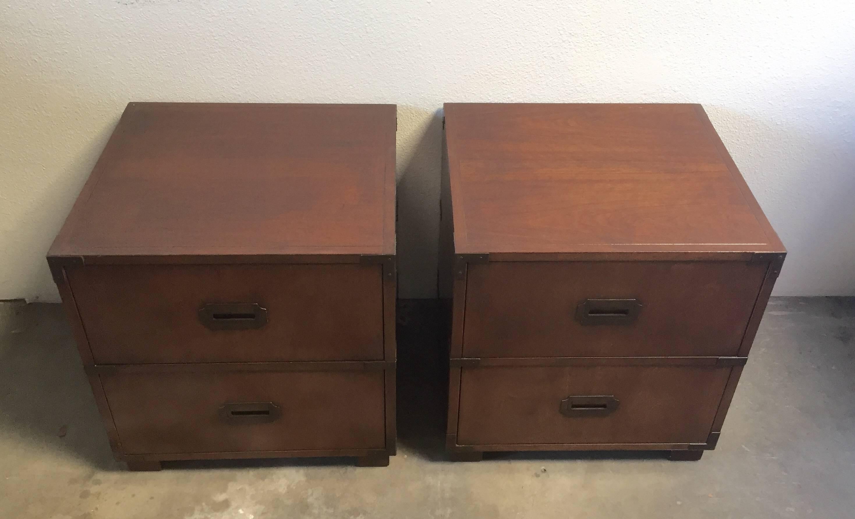 Pair of Baker Campaign style side tables. Each table has two drawers: Top one with a fold down front and pull-out drawer below. Restrained with original aged brass accents. Maker's mark inside bottom drawer of both tables.