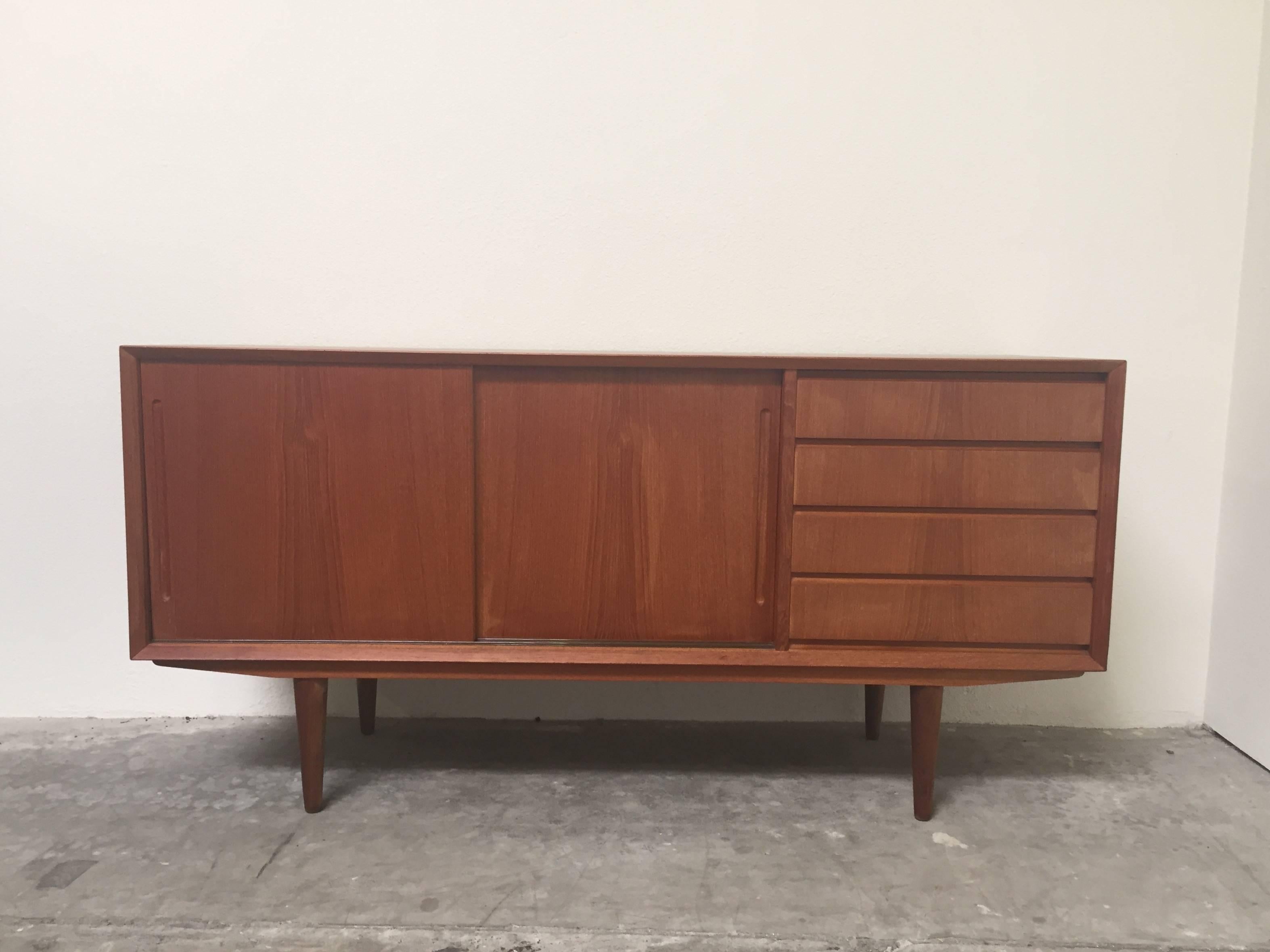 Fantastic Mid-Century Modern Danish teak sideboard in excellent vintage condition. Four drawers and two slider doors that open to two shelf compartments. Top drawer is lined with felt. The right side of the credenza has some small blonde spots, part