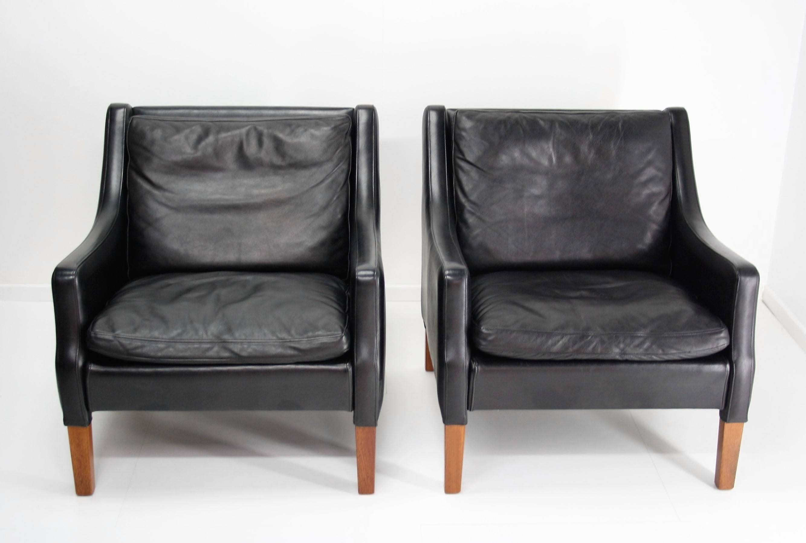 Pair of easy chairs with a solid teak frame and tufted beautiful patinated black leather cushions. 
The patinated leather is very desirable in combination with the teakwood.