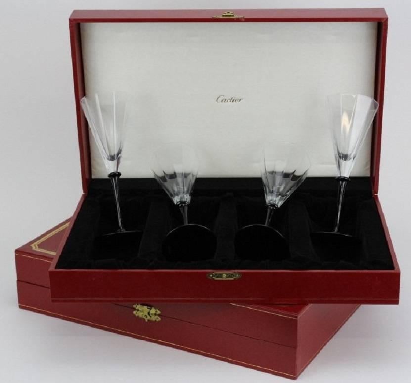 Set of eight signed Cartier champagne glasses or flutes in their original Cartier red boxes. Crafted of fine quality French crystal with black crystal stems. Art Deco paneled design. Each signed Cartier. Each measures 8 1/2