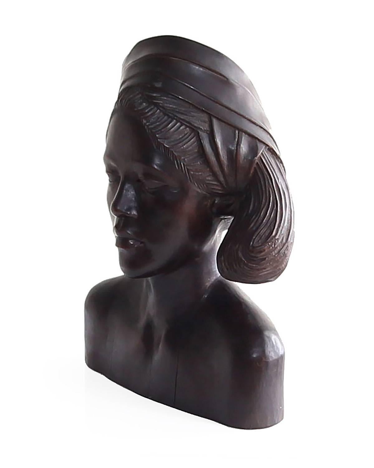 Beautiful carved mahogany wood bust of an Balinese woman wearing a headscarf. This piece is a fine example of traditional wood carving techniques. Powerful specimen with a lot of visual interest and presence. Circa 1950's.


