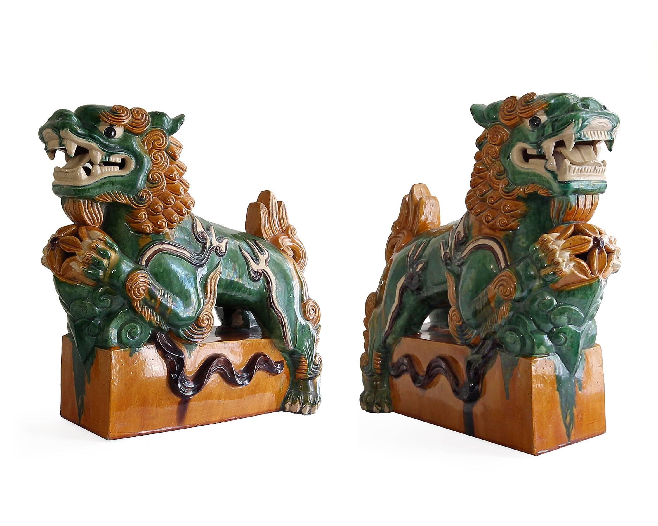 Extremely decorative and colorful pair of Chinese Sancai glazed statues in the form of foo dog lions on resting on pedestals with a ball in their front paws. Each in a mirrored format with open jaws.

Each measures approximately 18