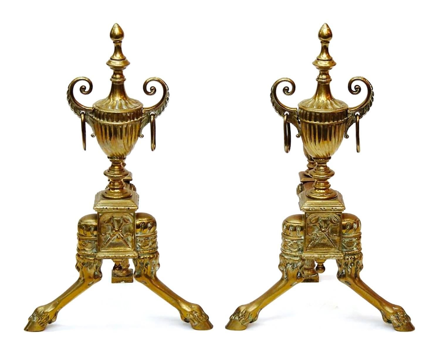 They don't get more neoclassical in style than these gorgeous andirons! In the form of large ribbed urns with curving, ring-attached open handles and topped with a flame finial on waisted socle, resting on a crossed horns-embossed base from which